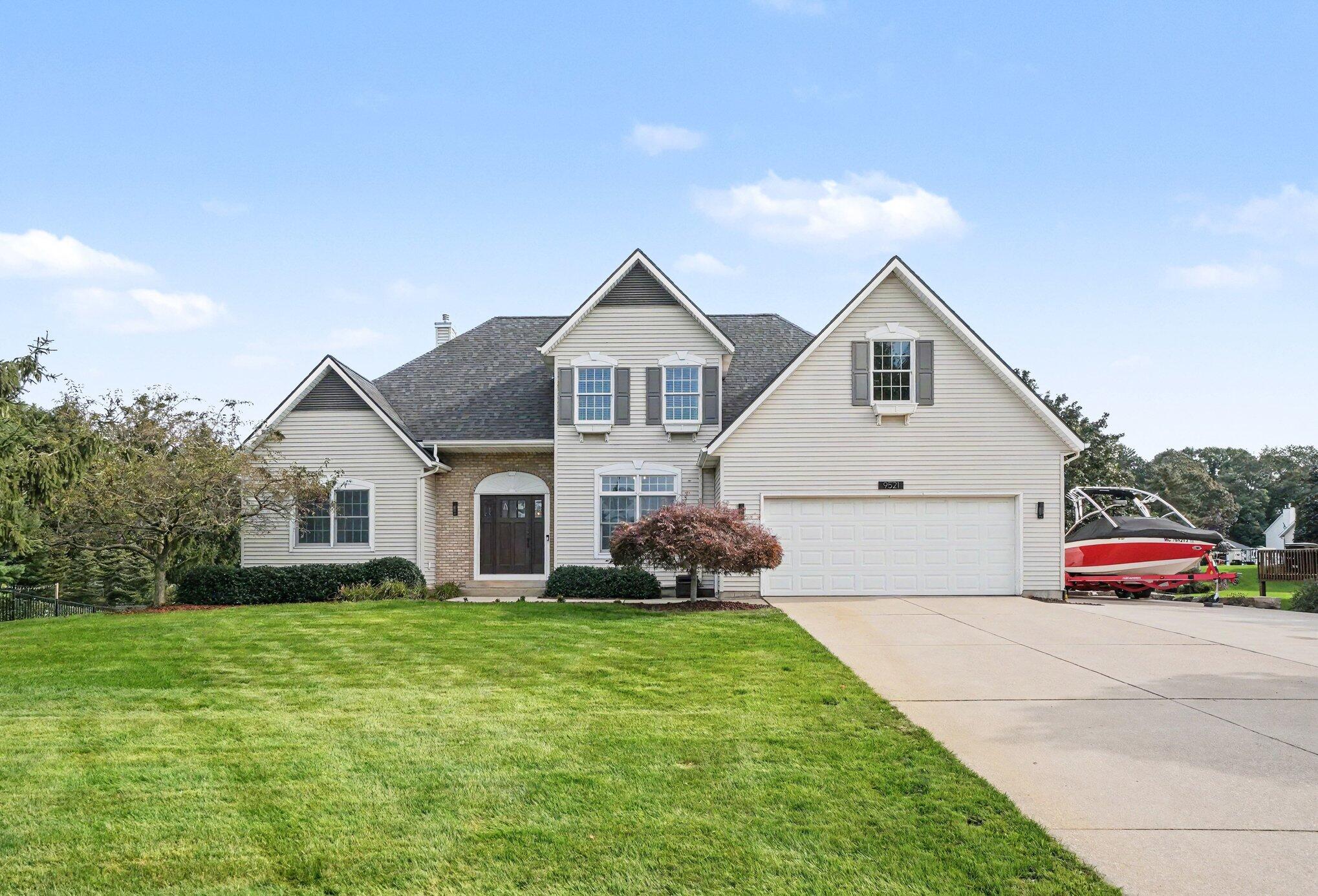 Two-story house with a brick entry, attached garage, broad lawn, and a boat beside the driveway.