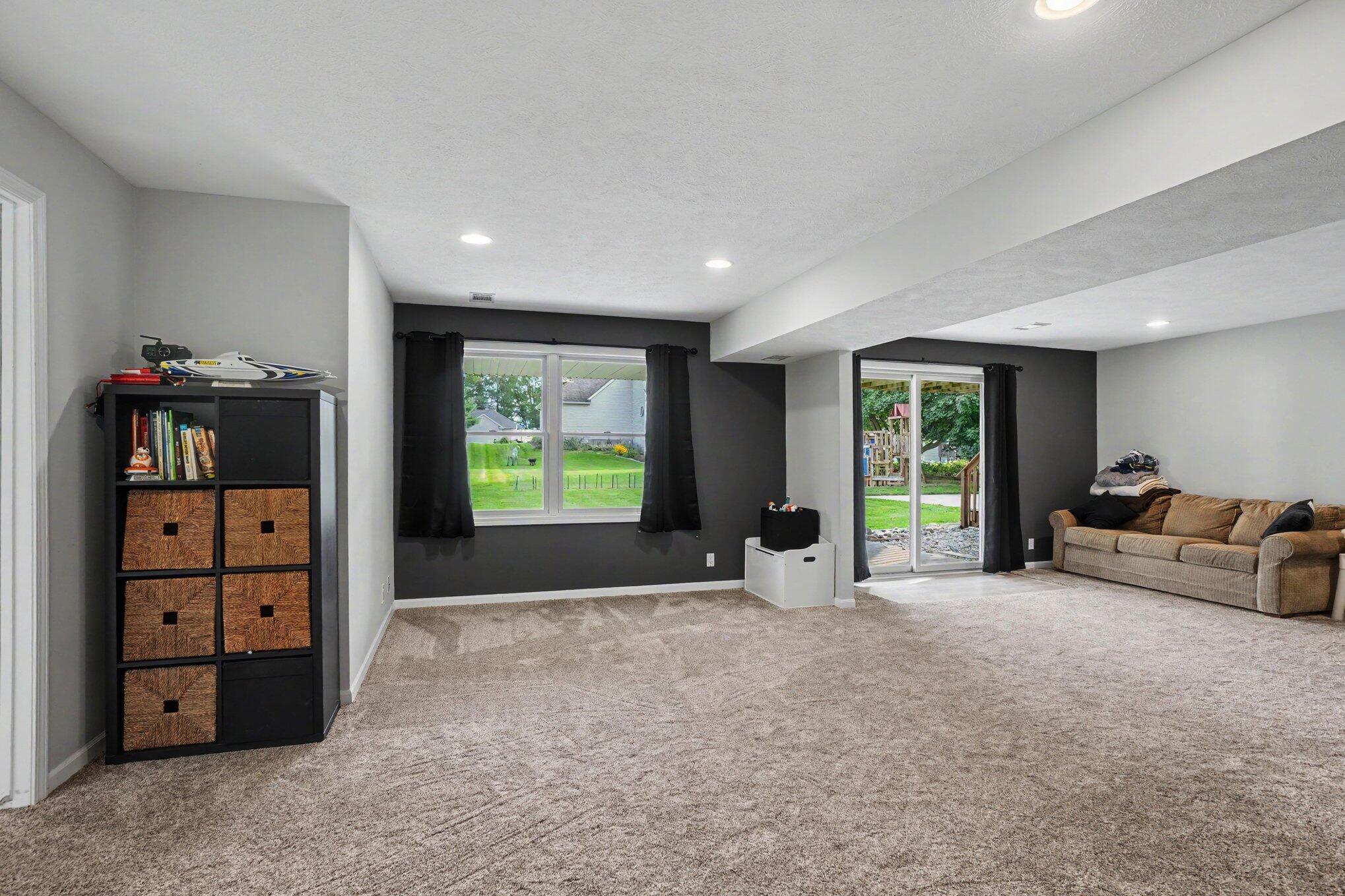 Basement family room with beige carpet, a brown sofa, and sliding glass doors to the backyard.