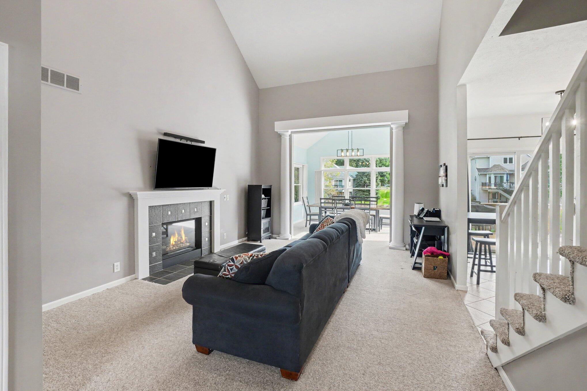 Vaulted living room with a dark sofa, gas fireplace, and bright dining area beyond.