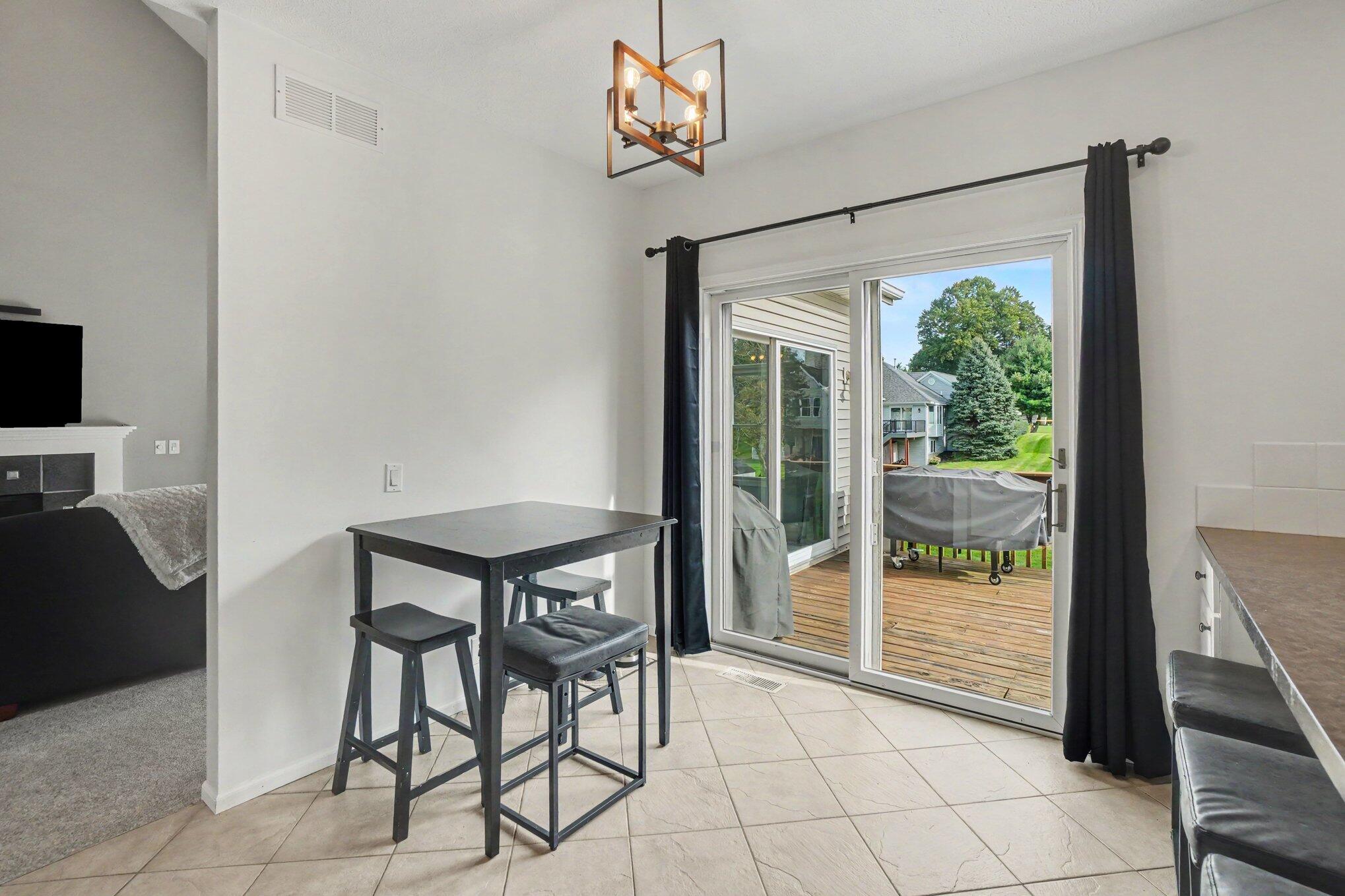 Dining area with black table and stools beside sliding doors to a deck and green yard.