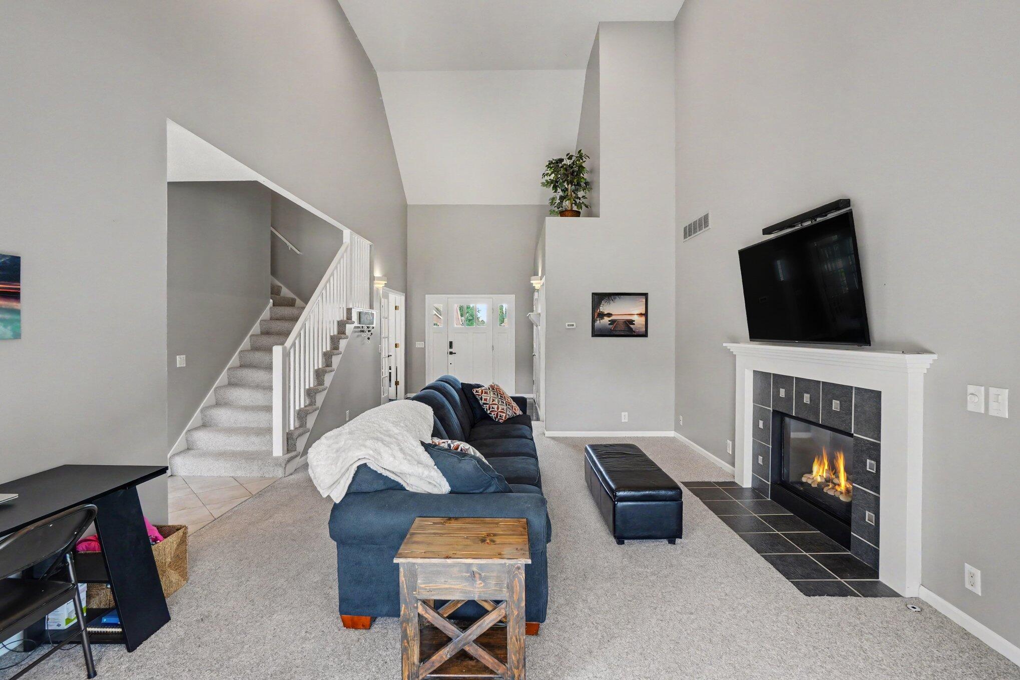 Furnished living room with a blue sectional, vaulted ceiling, carpeted staircase, and fireplace.