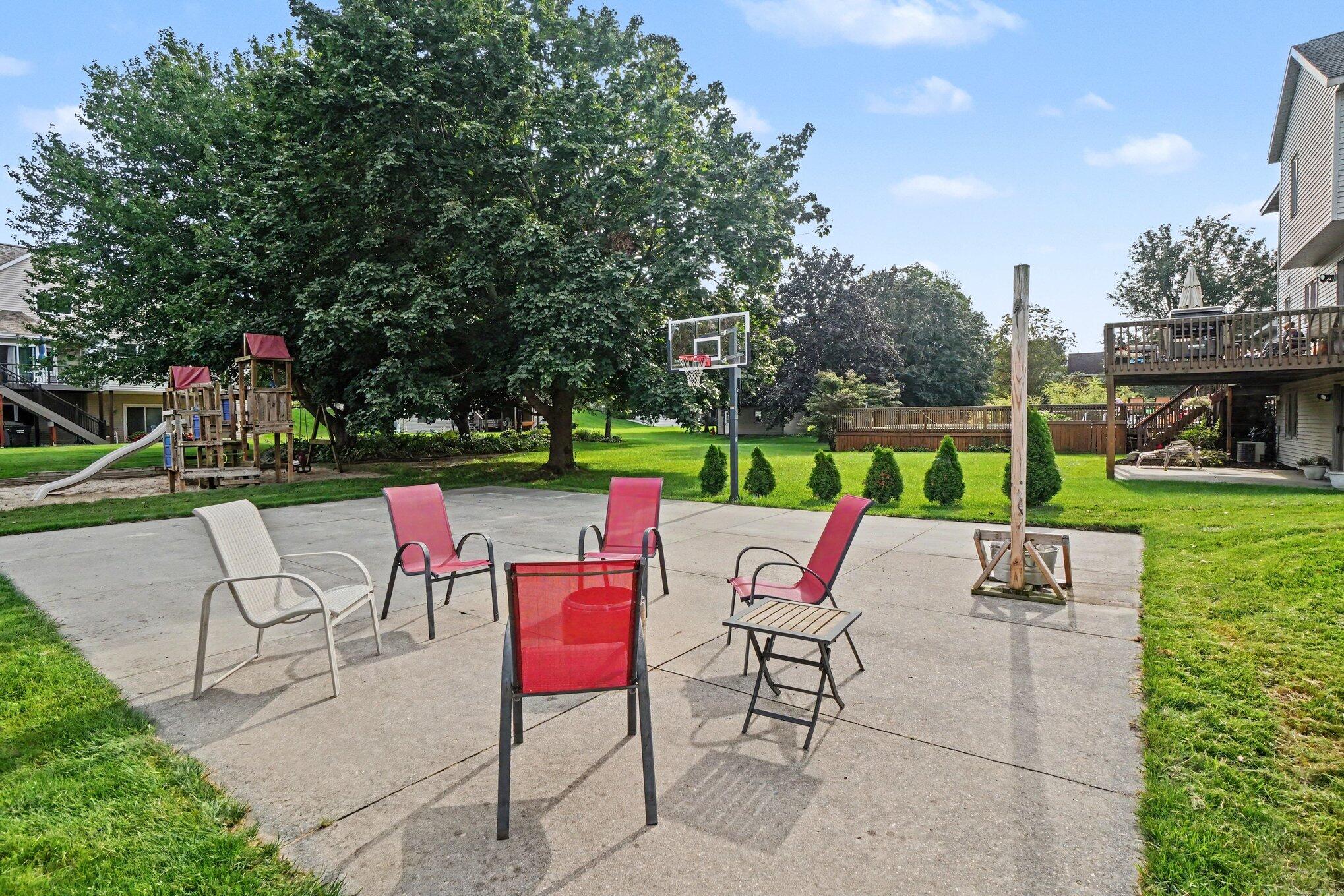 Backyard patio with colorful seating, a basketball hoop, and a children’s playset.