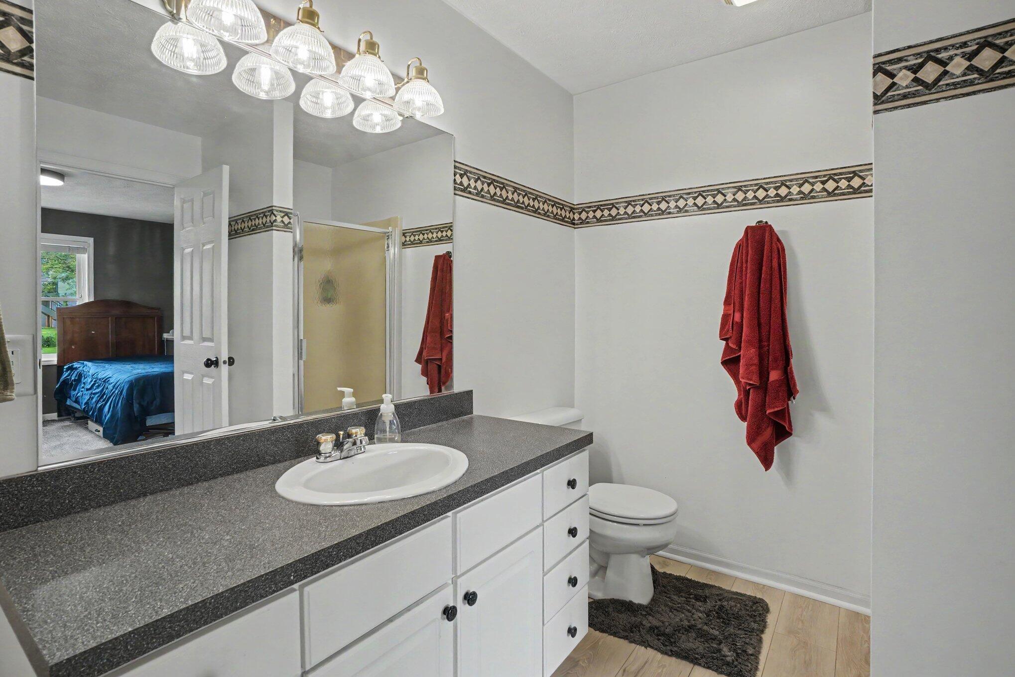Bathroom with a long gray vanity, oval sink, toilet, patterned wall border, and red towels.