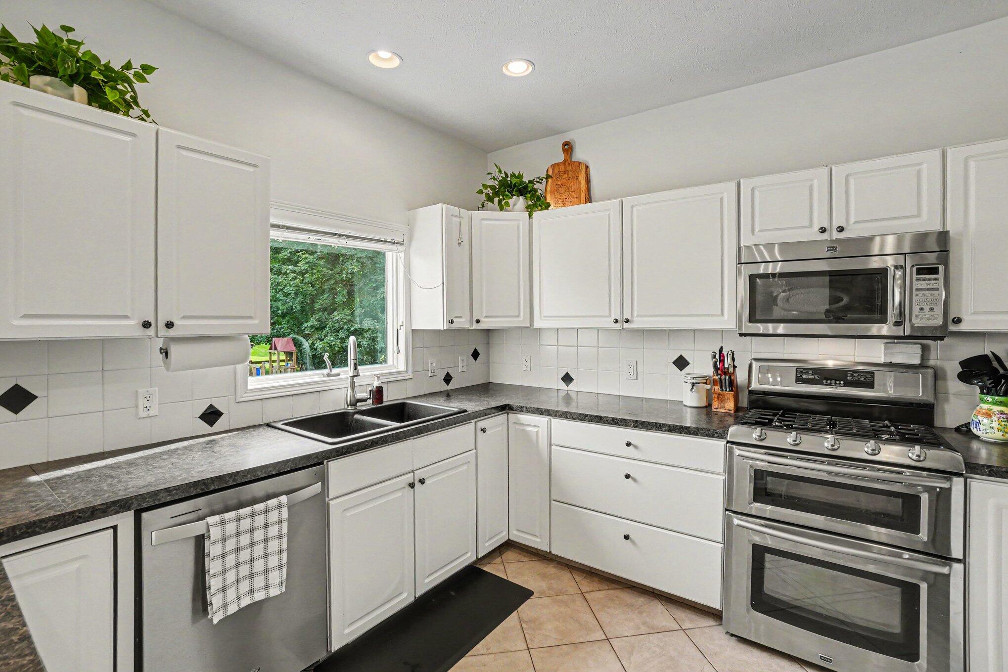 Kitchen with white cabinets, dark countertops, a window over the sink, and stainless-steel appliances.