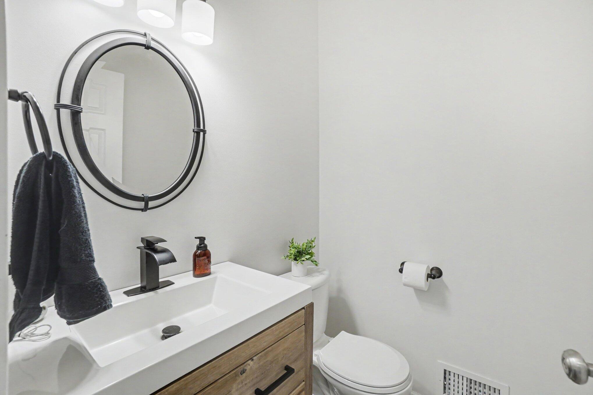 Bathroom with a wood-front vanity, oval mirror, black fixtures, and toilet.