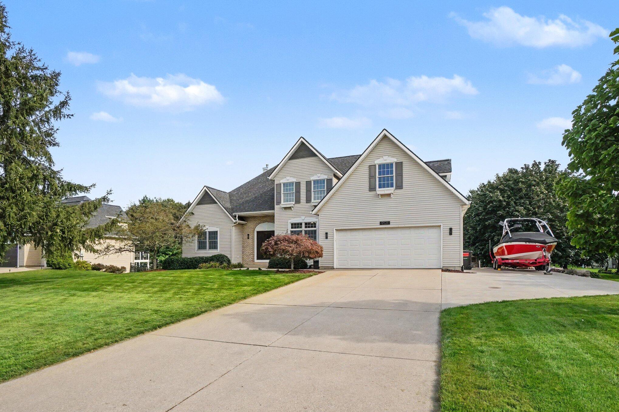 Two-story beige house with a two-car garage, broad driveway, and boat parked beside it.