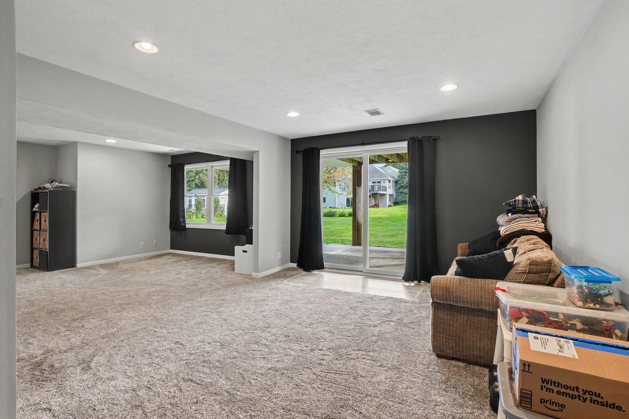 Carpeted living room with sliding patio doors, a dark accent wall, and a sofa beside moving boxes.