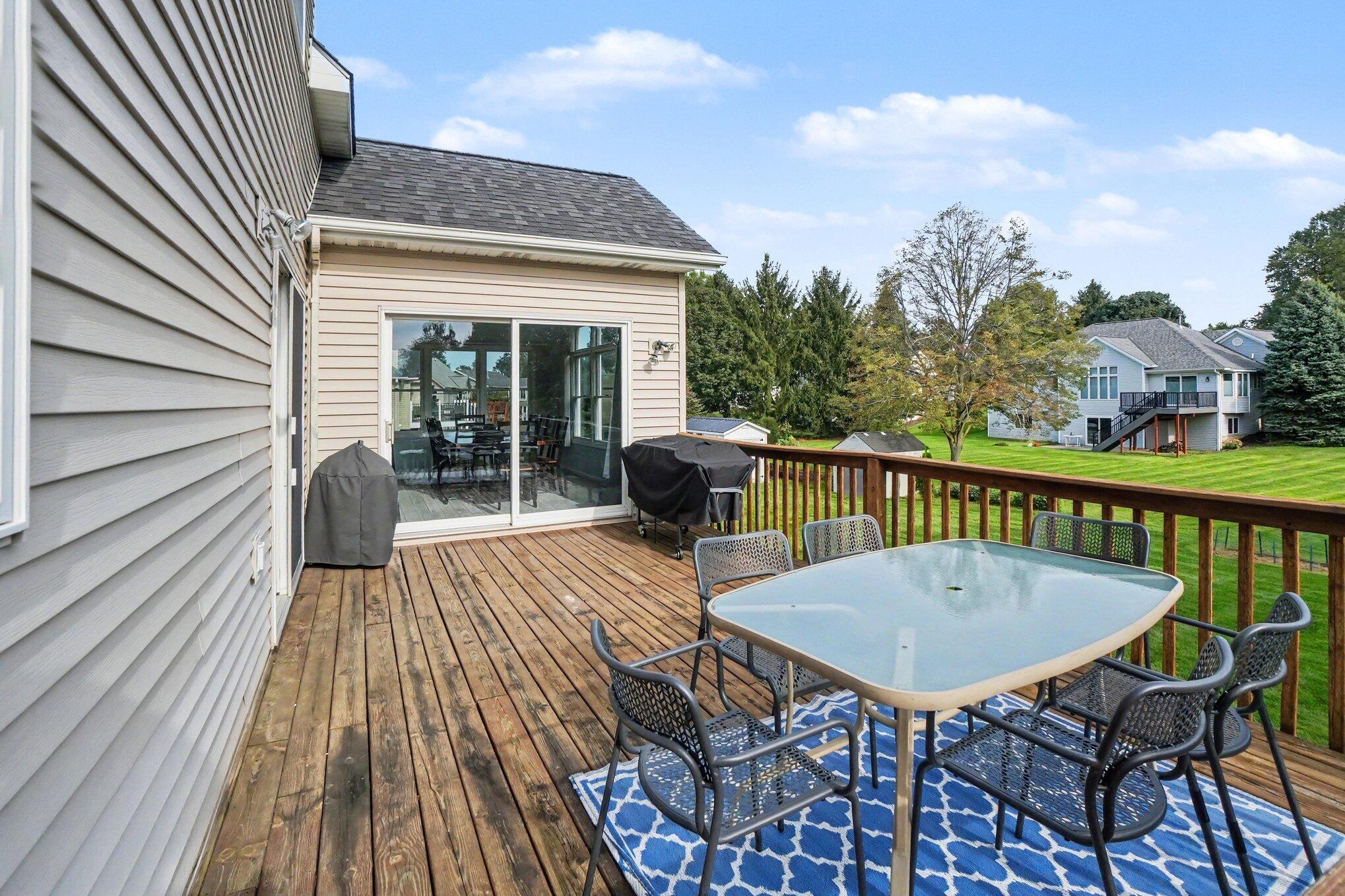 Wooden deck with outdoor dining set overlooking a green lawn.