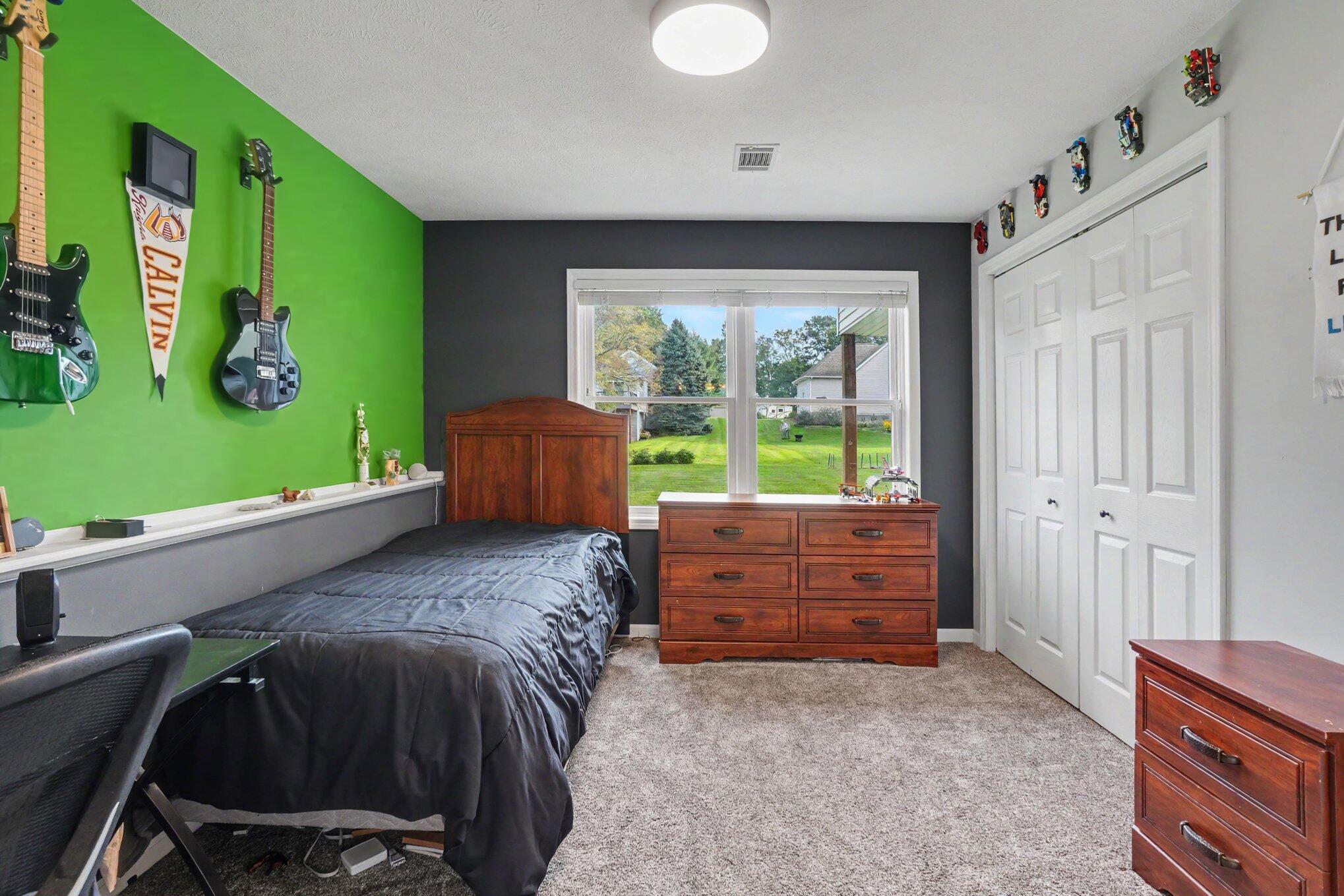 Bedroom with a vivid green guitar-display wall, dark bedding, and a large window overlooking the lawn.