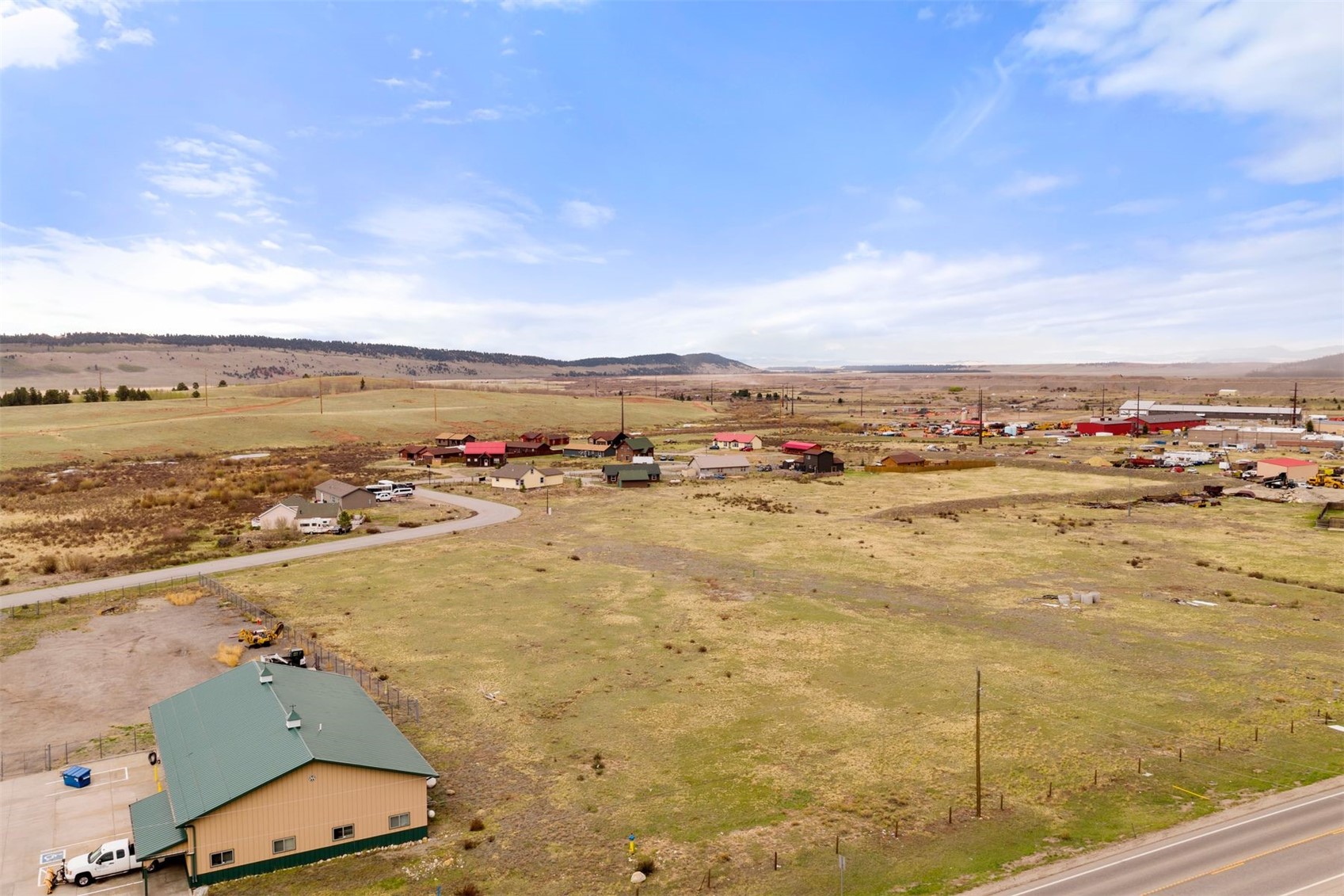 Aerial view of open land beside US-285, with scattered buildings and low hills in the distance.