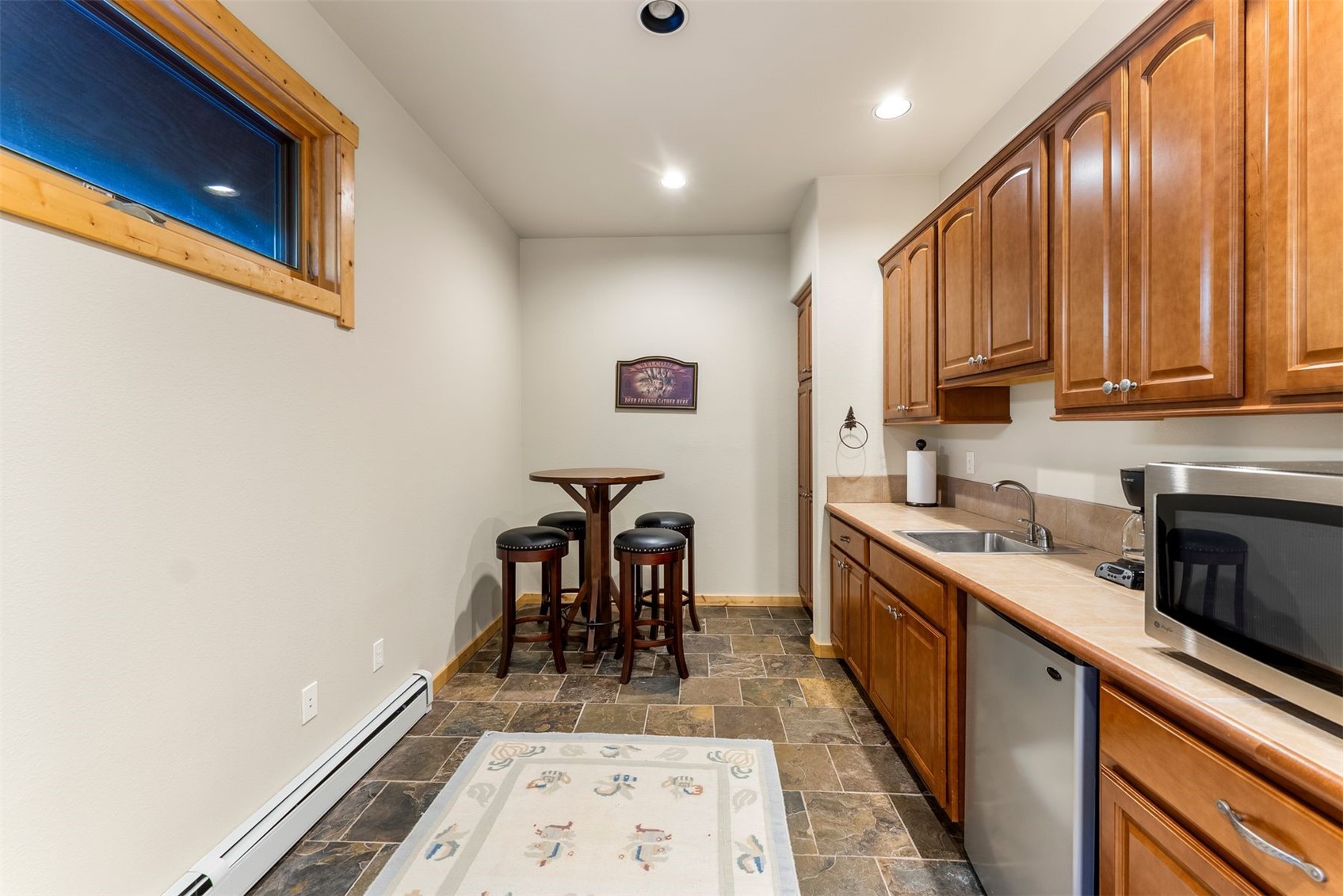 Compact kitchen with warm wood cabinets, slate-look tile floor, and a round table with stools.