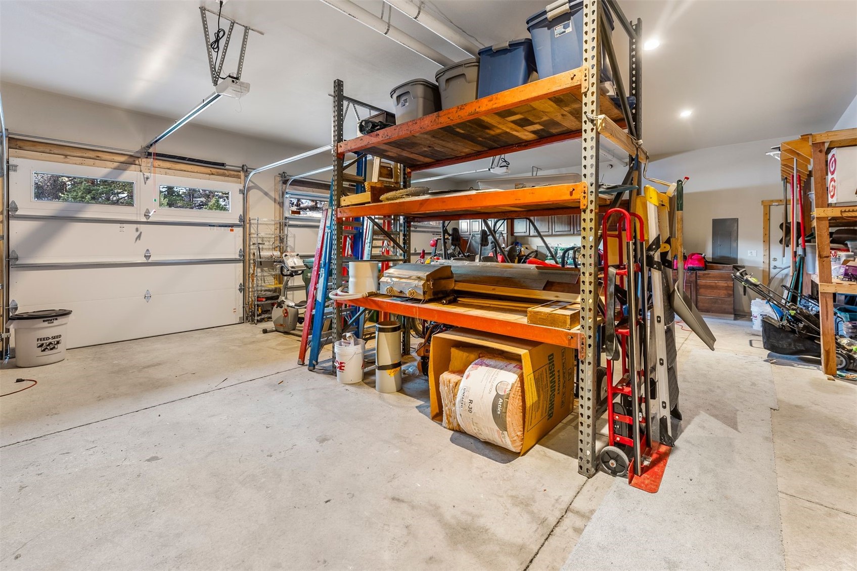 Garage interior with storage racks, bins, ladders, and two garage doors.