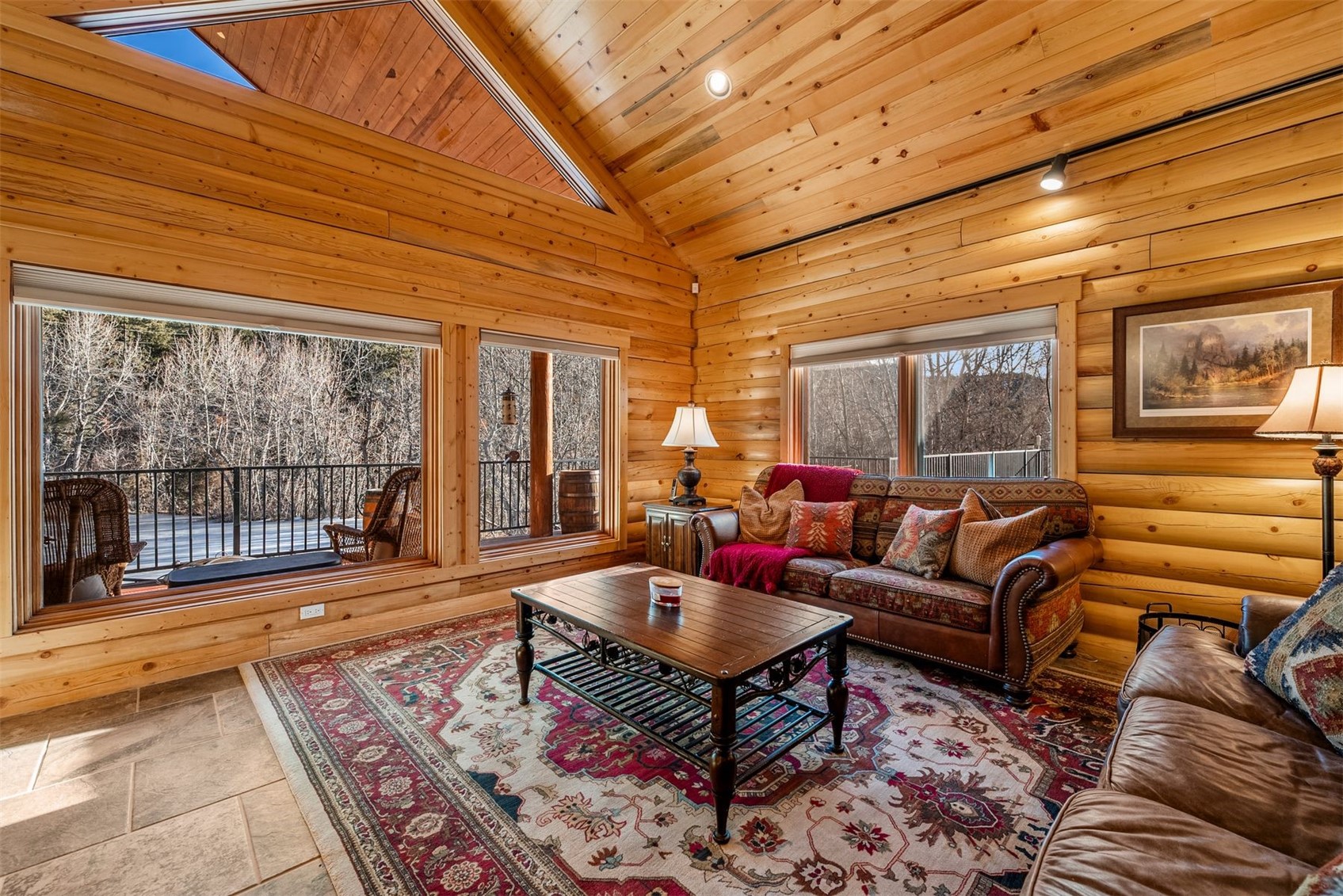 Wood-paneled living room with a vaulted ceiling, large windows, leather seating, and a patterned rug.