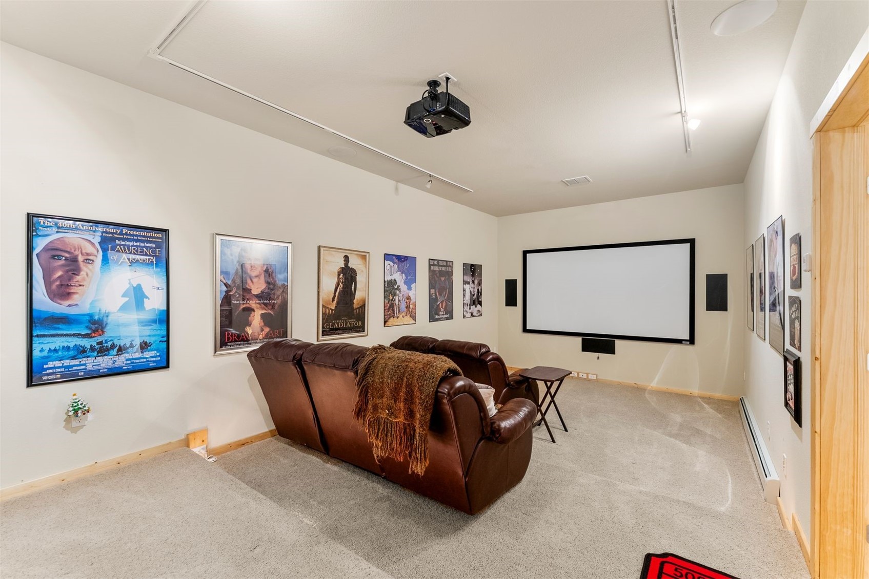 Home theater with a projection screen, ceiling-mounted projector, movie posters, and brown leather seating.