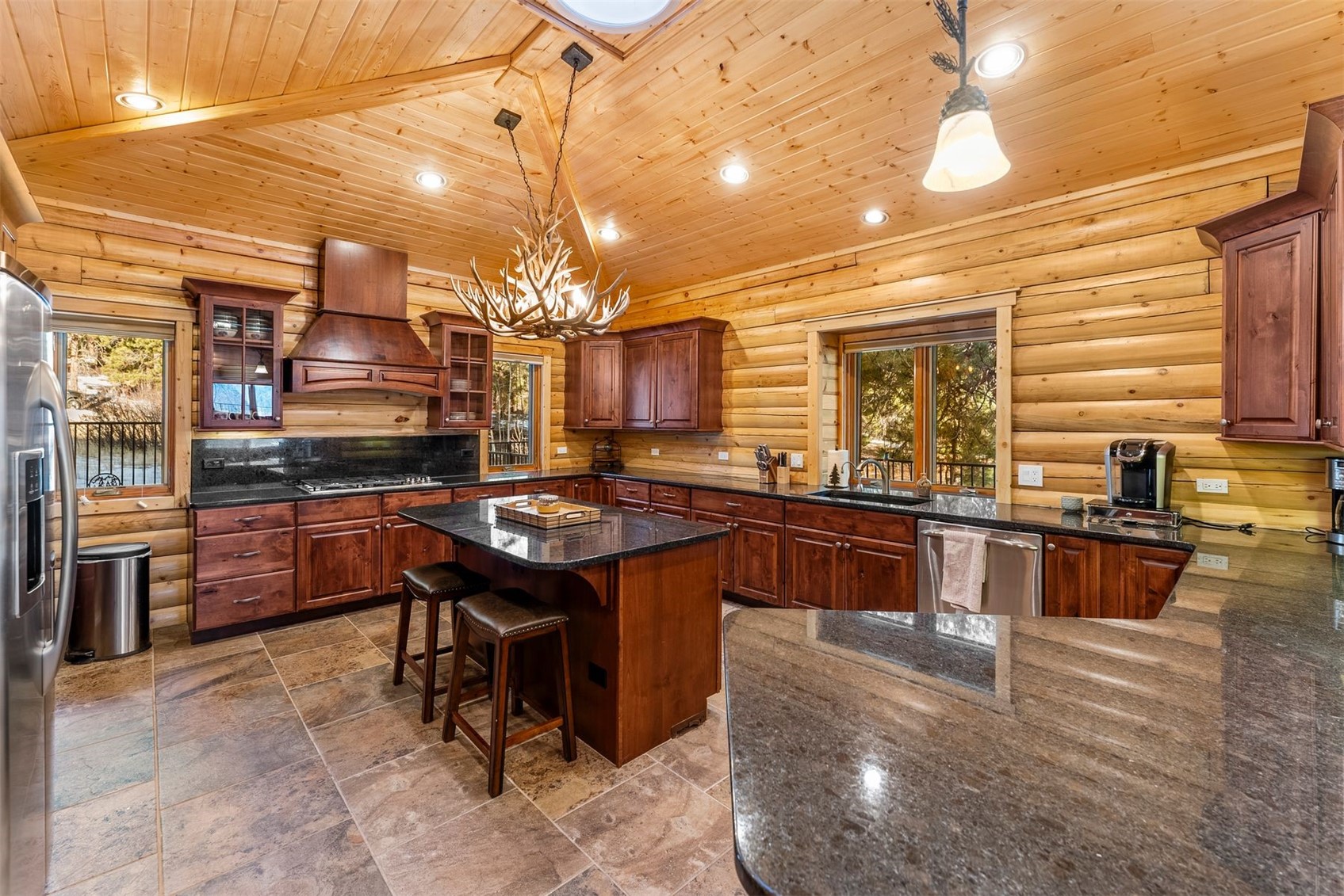 Log-cabin kitchen with a granite island, cherry cabinets, and an antler chandelier.