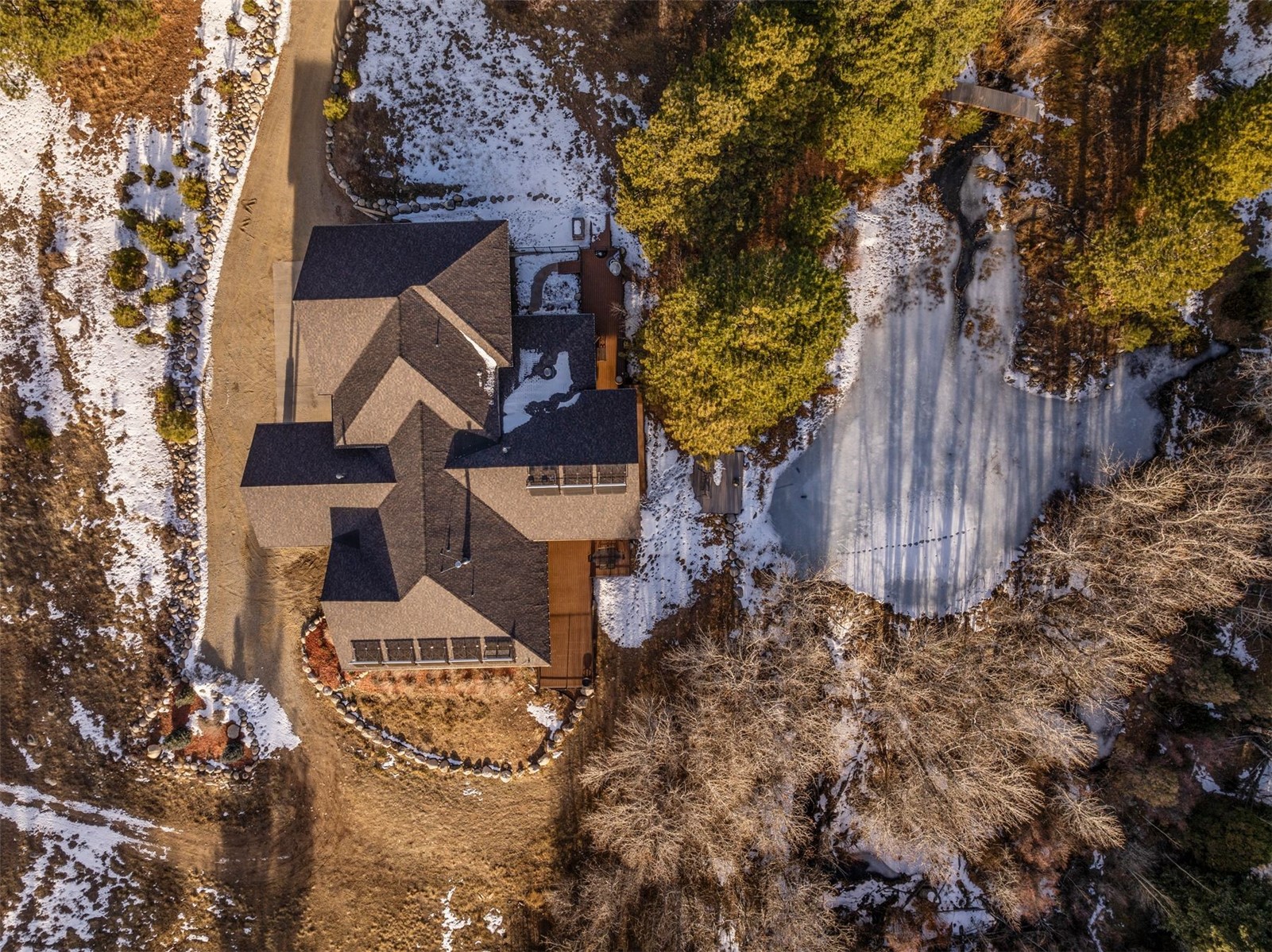 Aerial view of a large home beside a curved driveway, evergreens, and patchy snow.