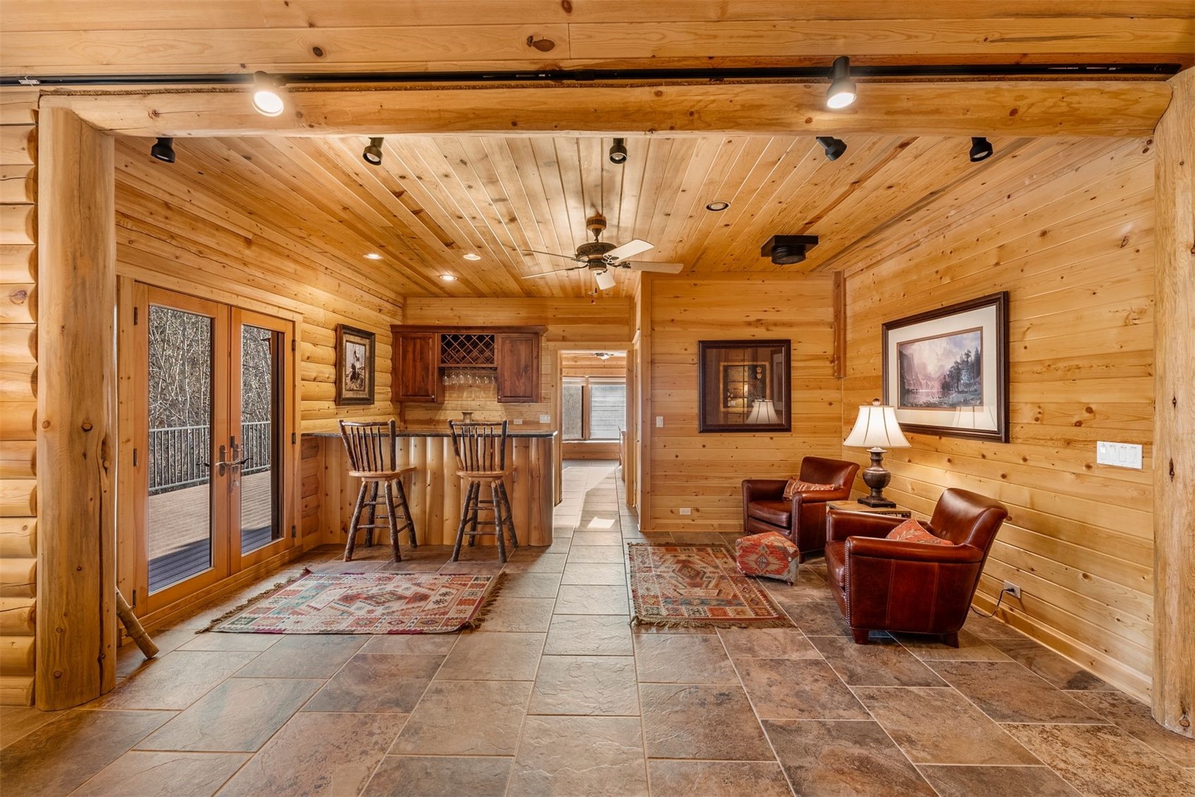 Log-cabin living area with a bar, leather armchairs, and glass doors to a deck.