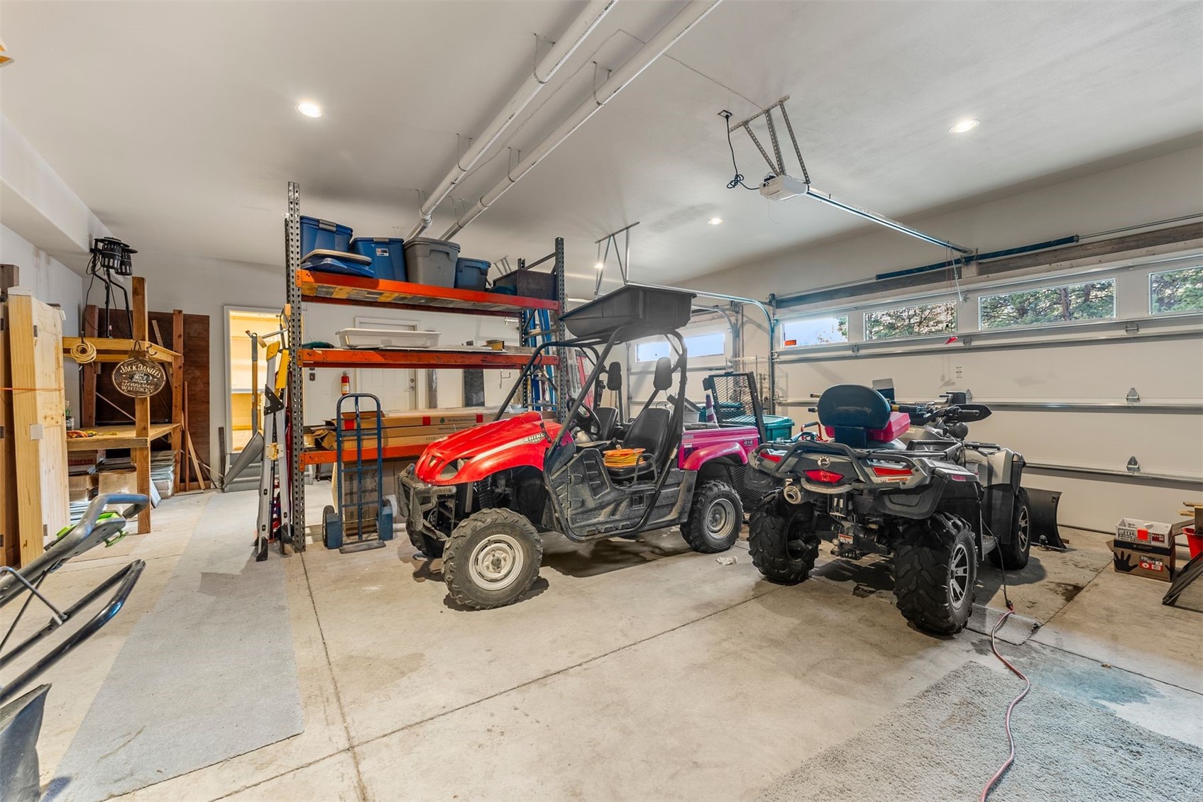 Spacious garage with storage racks and several off-road vehicles, including a red side-by-side.