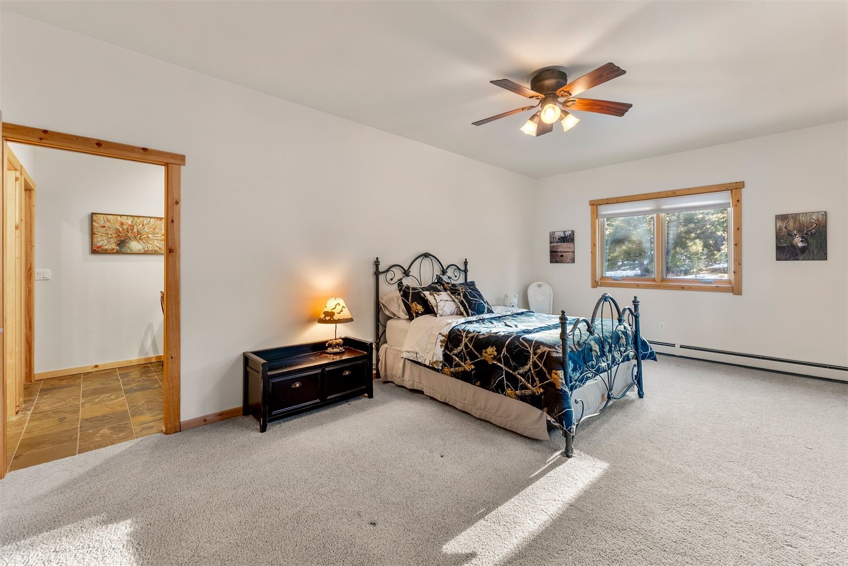 Bedroom with a black metal bed, blue patterned quilt, wood-trimmed window, and ceiling fan.