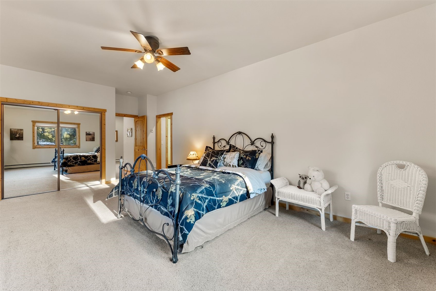 Bedroom with a black metal bed, blue floral bedding, mirrored closet doors, and white wicker chairs.