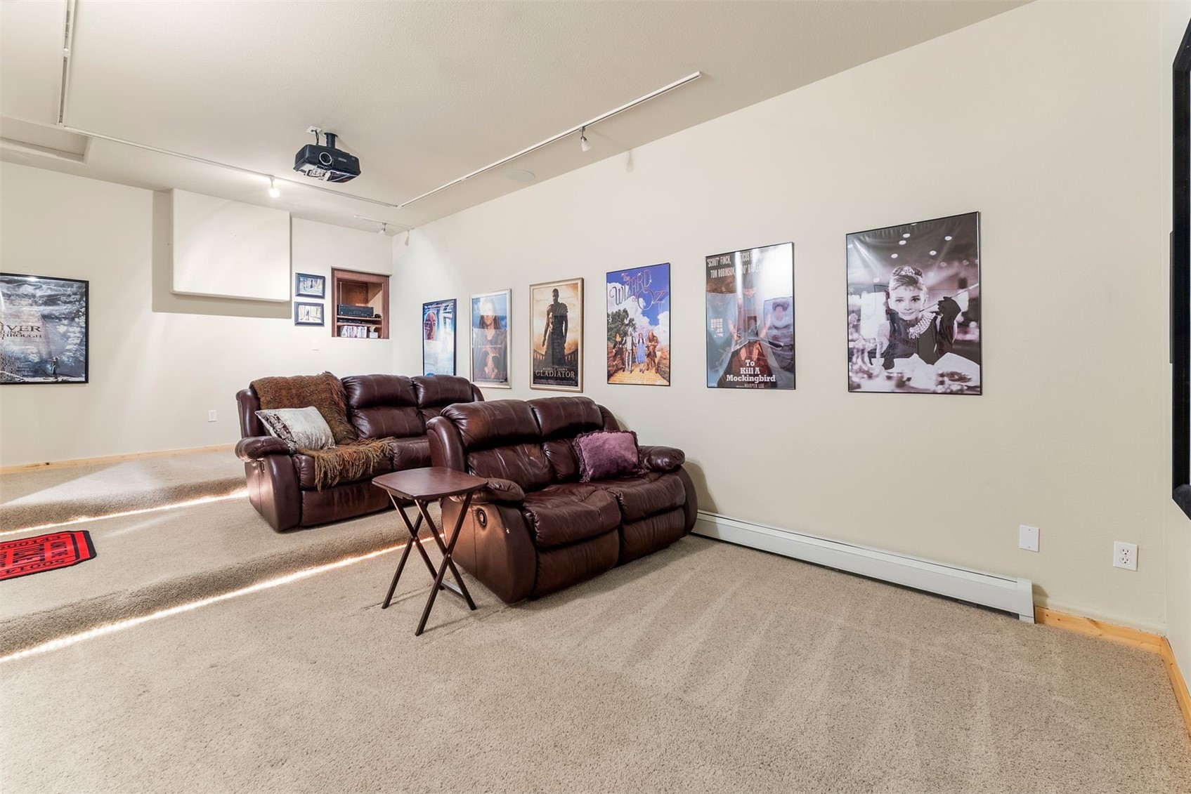 Furnished media room with leather reclining sofas, a ceiling-mounted projector, and framed movie posters.