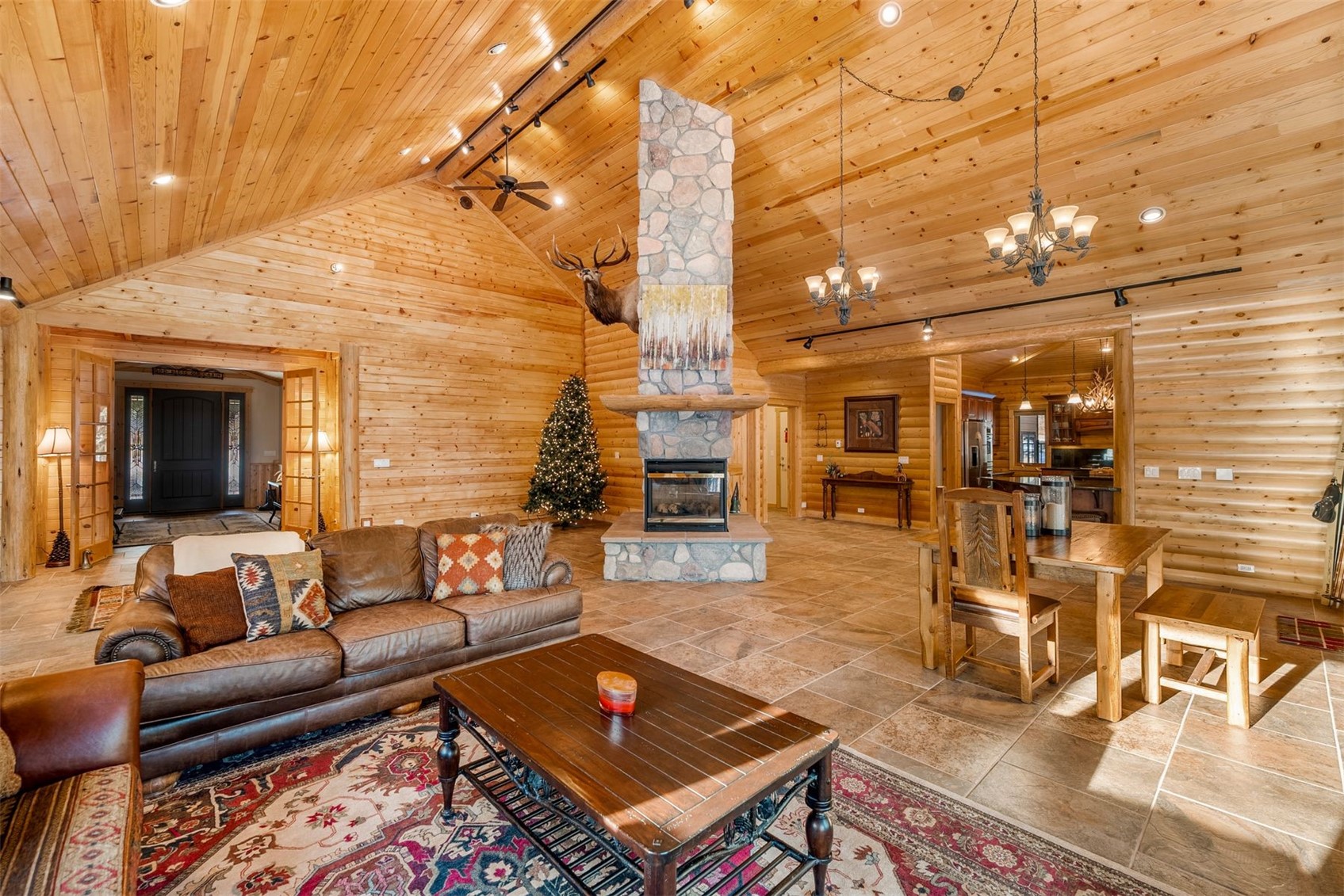 Great room with vaulted wood ceiling, stone fireplace, leather seating, and adjoining dining area