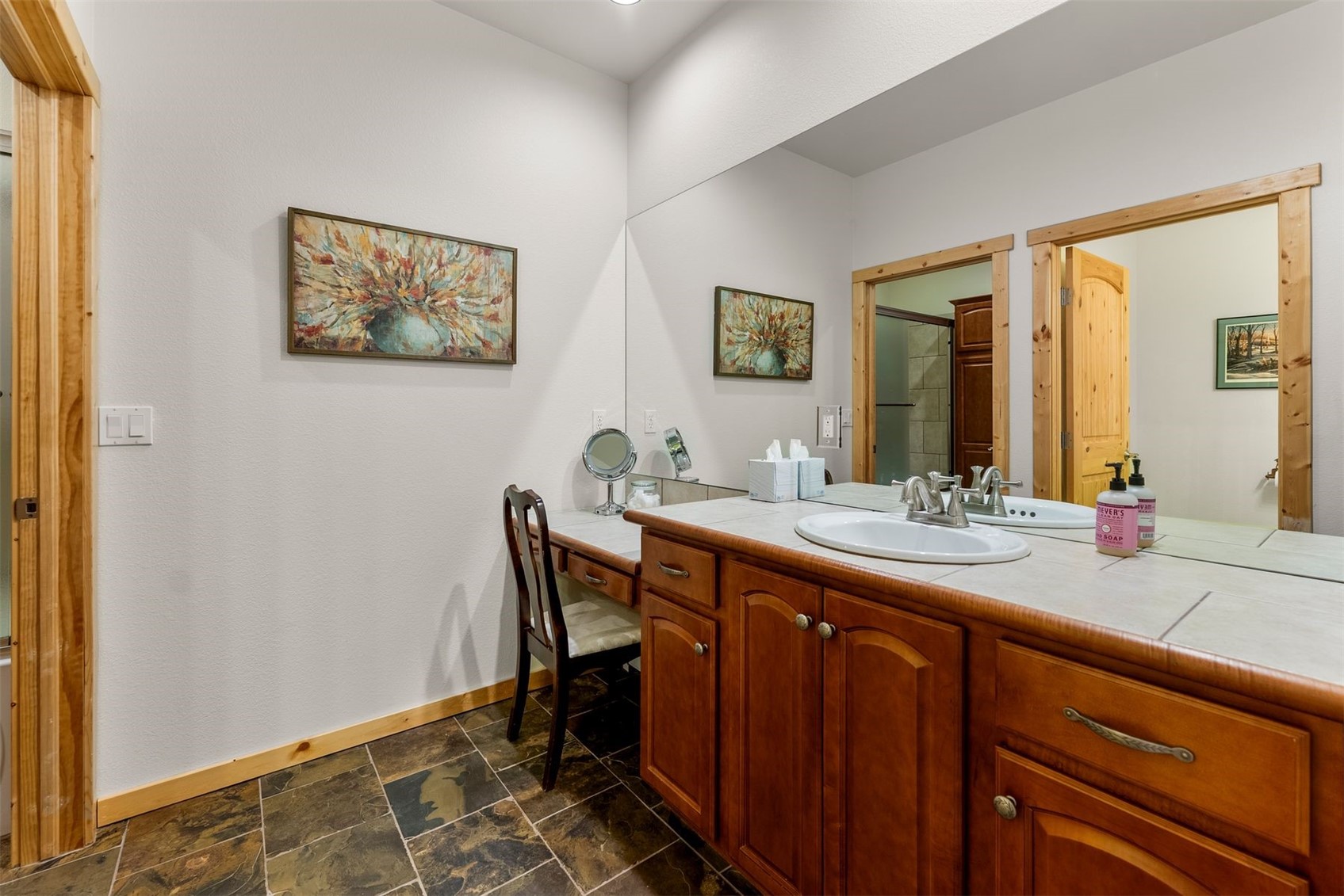 Bathroom with wood cabinetry, a tiled vanity, large mirror, and a chair at the makeup desk.