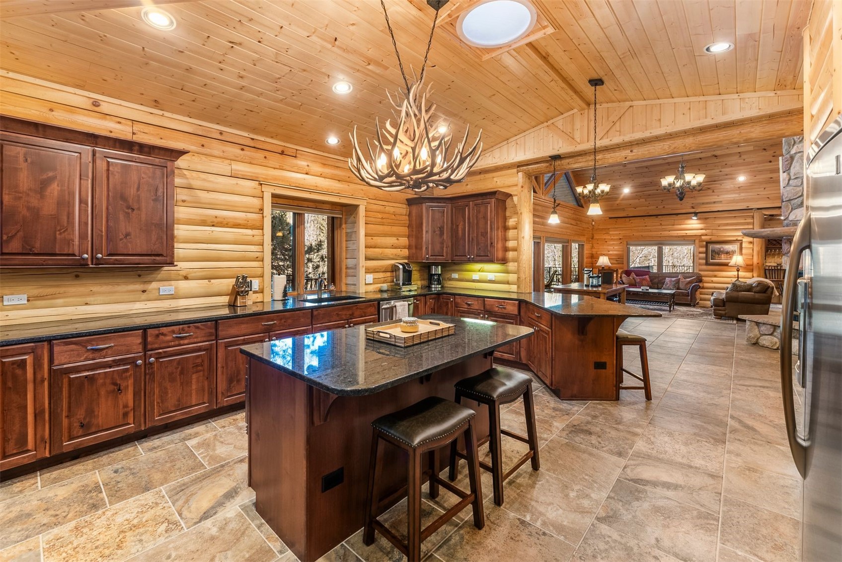 Log-cabin kitchen with a granite island, dark wood cabinets, and an antler chandelier.