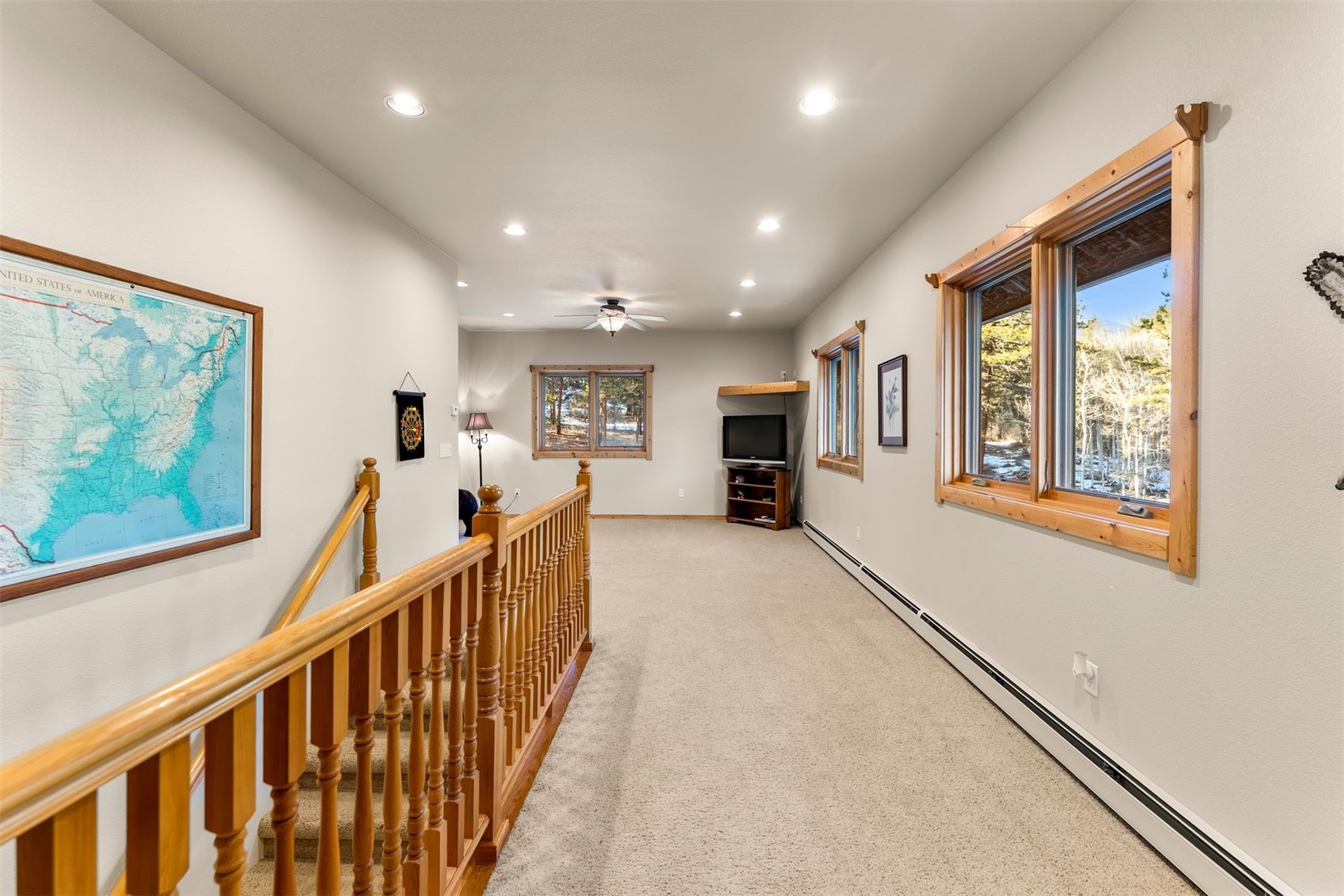 Carpeted upstairs hallway with a wooden stair railing and windows overlooking snowy trees.