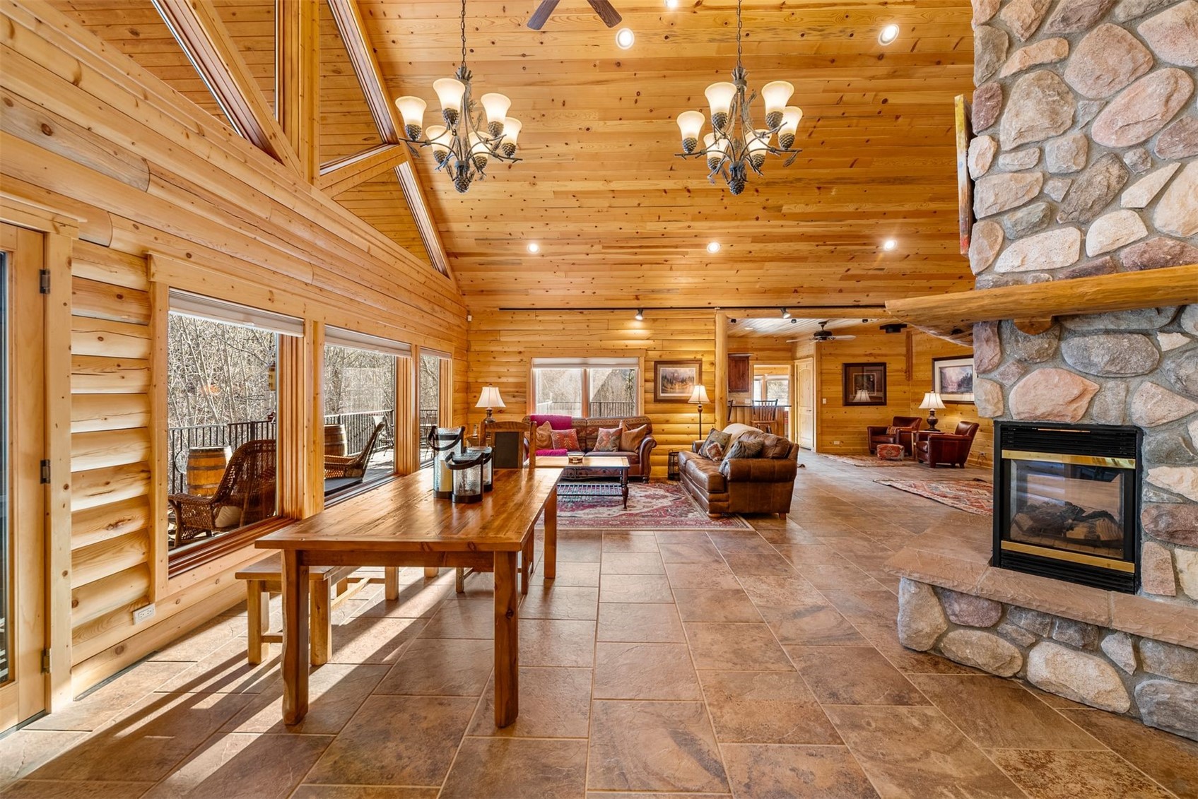 Furnished log-home living room with a vaulted pine ceiling and large stone fireplace.