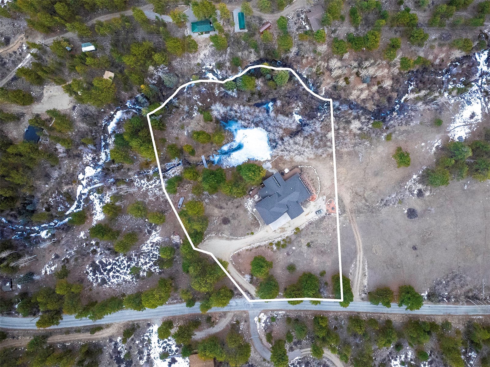 Aerial view of a rural home and pond within a white-outlined property, with trees and patches of snow.