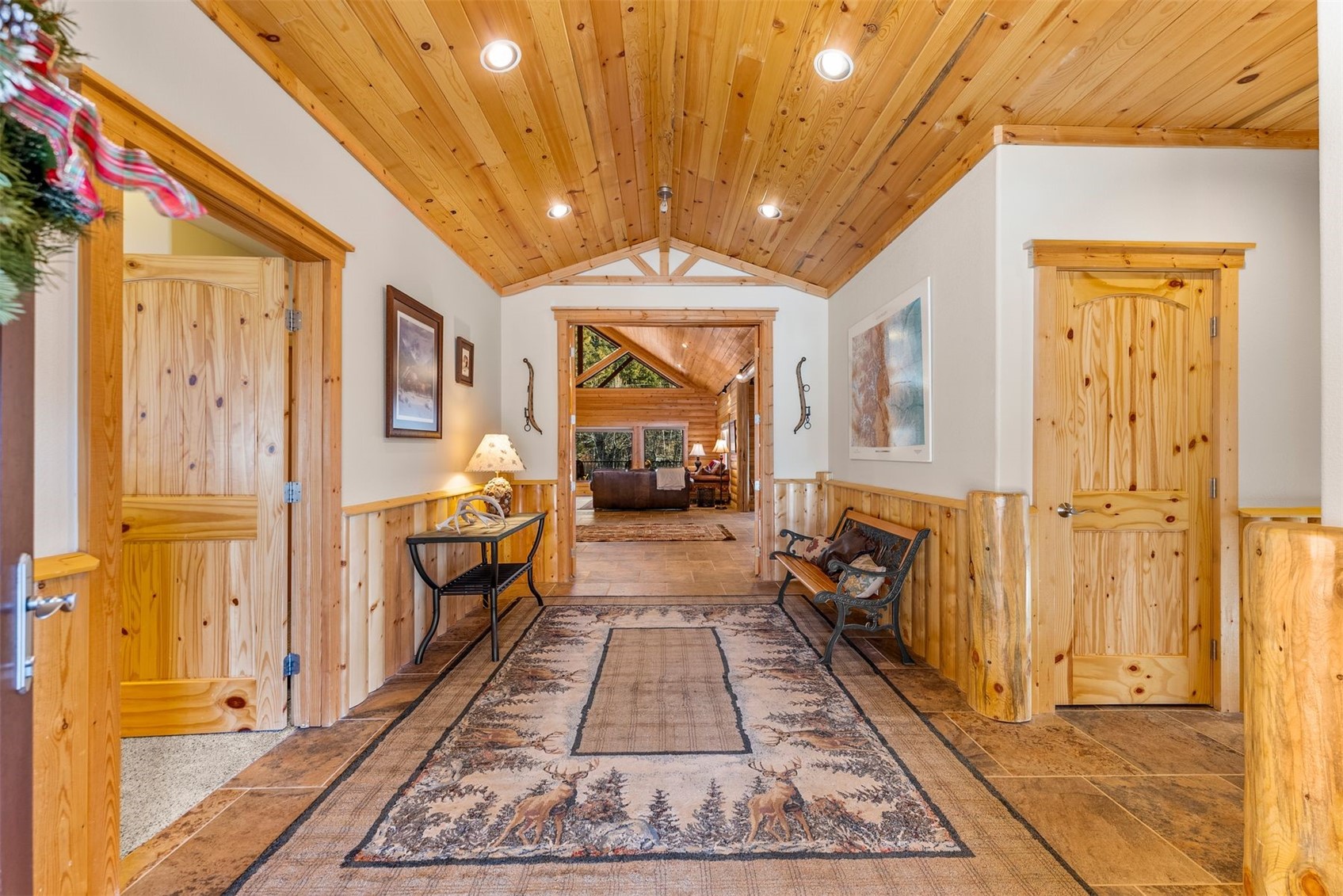 Entry hall with a vaulted pine ceiling, wood doors, tiled floor, and a patterned rug.