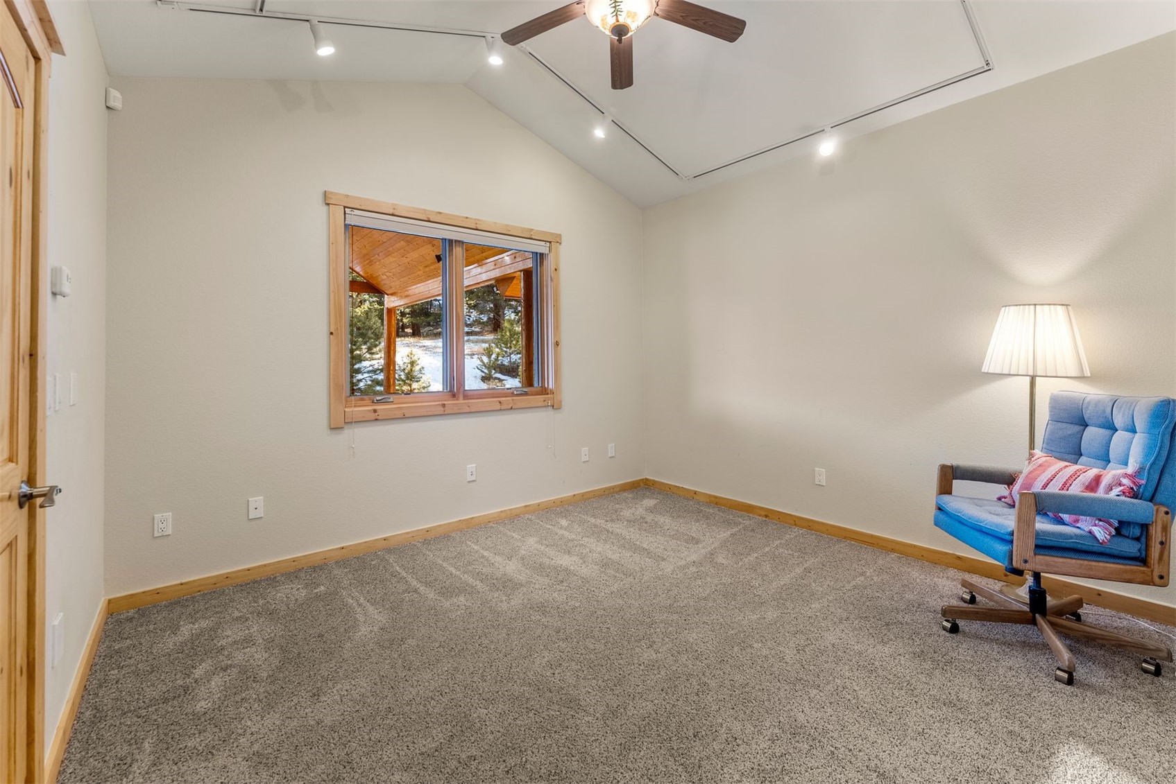 Carpeted room with a vaulted ceiling, wood-trimmed window, and blue rolling chair.