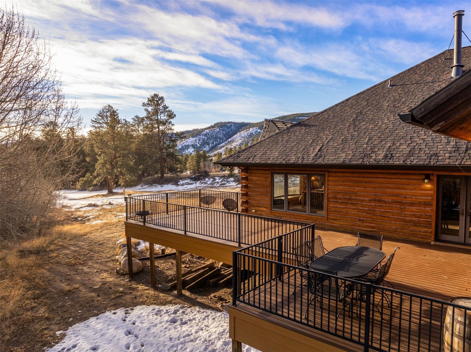 Log cabin decks with patio furniture overlook snow-dusted pines and mountain slopes.