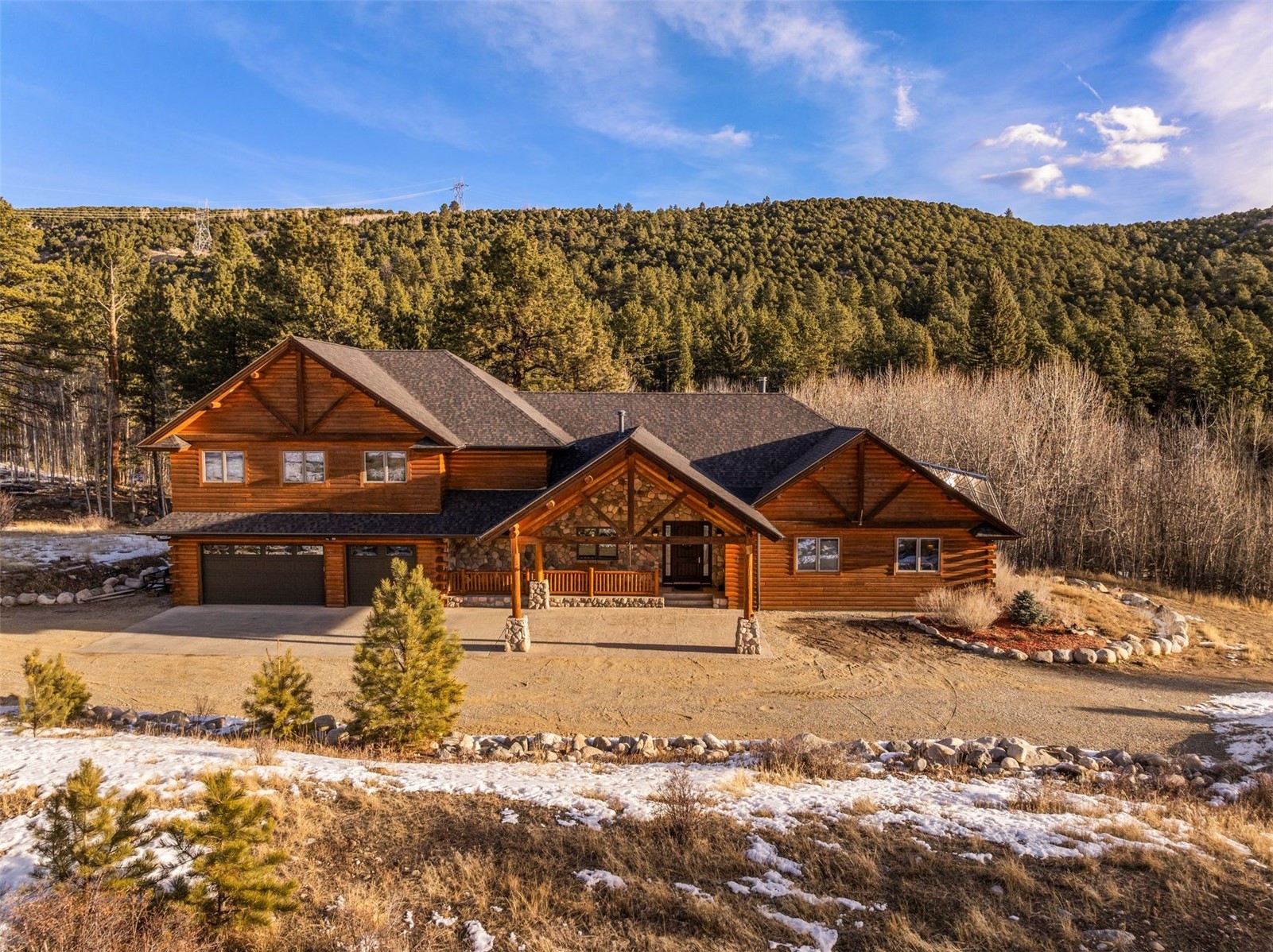 Log and stone home with multiple gables and a covered entrance, set against a wooded hillside.