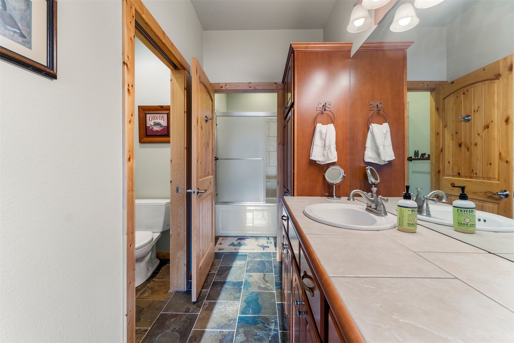 Bathroom with a long tiled vanity, wood cabinetry, and a tub-shower combination.