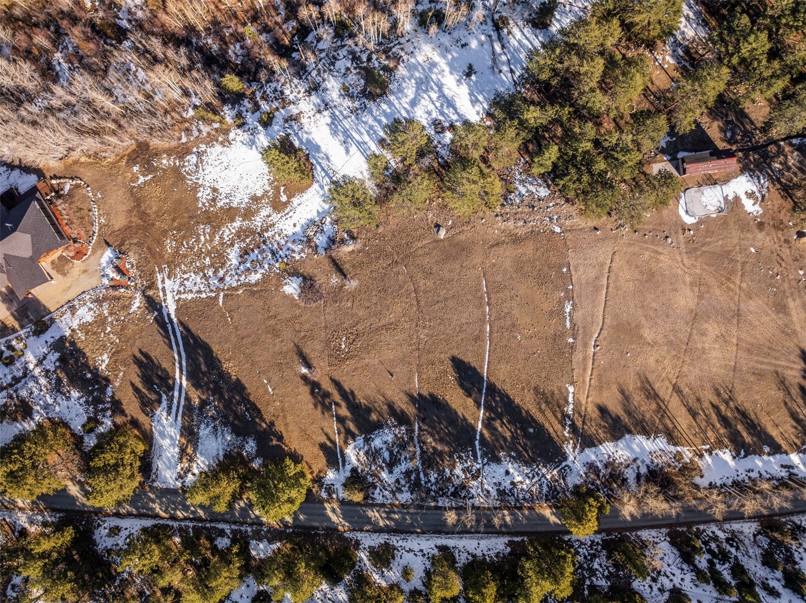 Aerial view of a snow-dusted, tree-lined property beside a road.