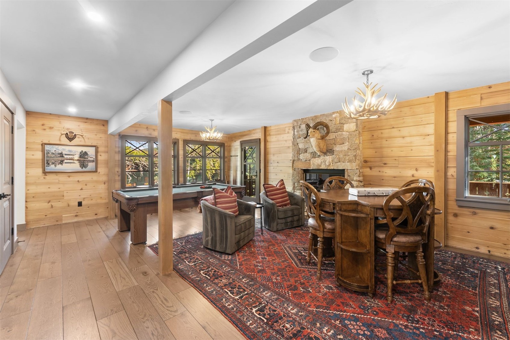 Dining and game room with a stone fireplace, round wooden table, pool table, and red patterned rug.