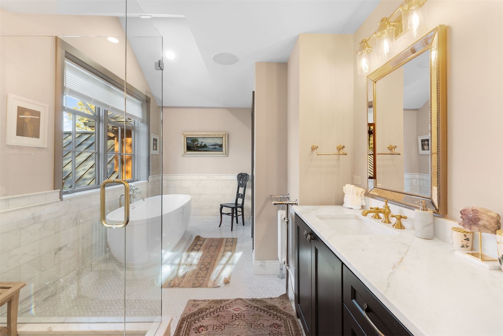Bathroom with a glass shower, freestanding tub, and marble-topped vanity with gold fixtures.