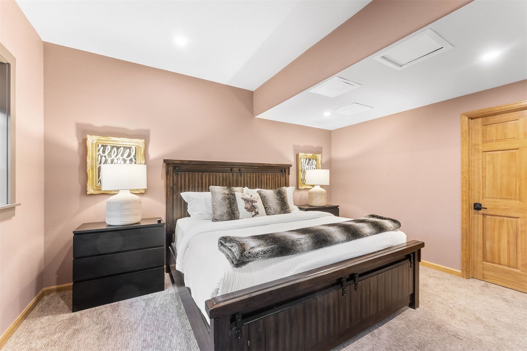 Furnished bedroom with a dark wood bed, white bedding, fur throw, and dusty pink walls.