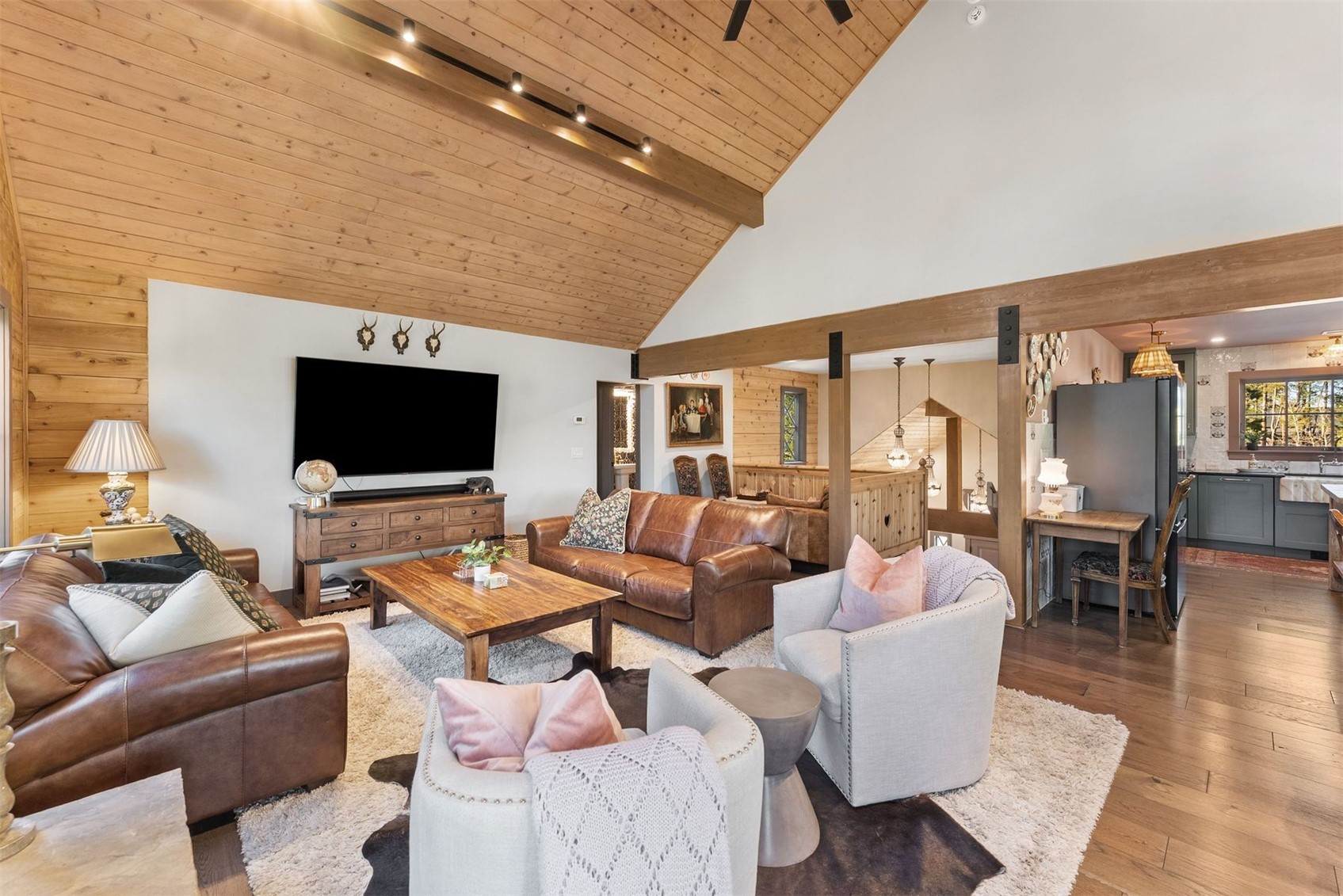 Living room with vaulted wood ceiling, leather sofas, and an open view to the kitchen.