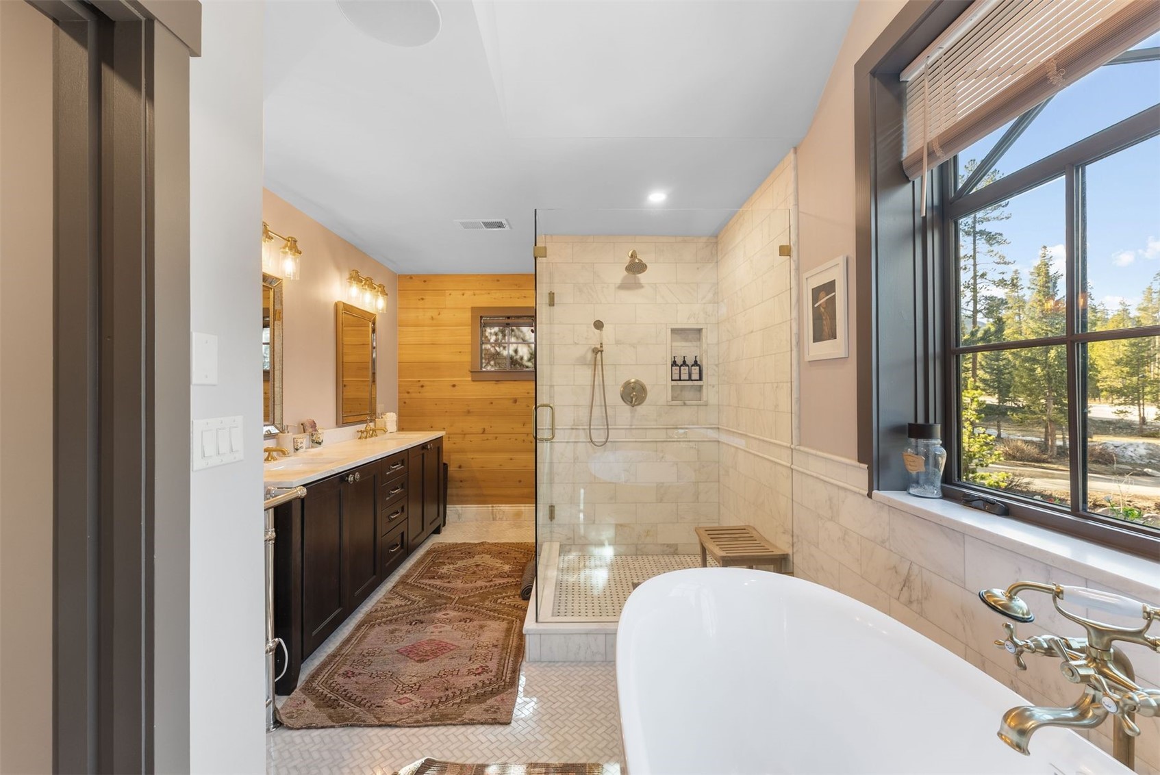 Bathroom with marble shower, freestanding tub, dark wood vanity, and a large window overlooking trees.