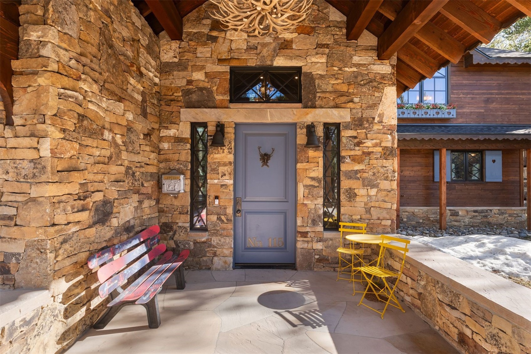 Stone entryway with gray No. 115 door, ski bench, and yellow patio furniture.