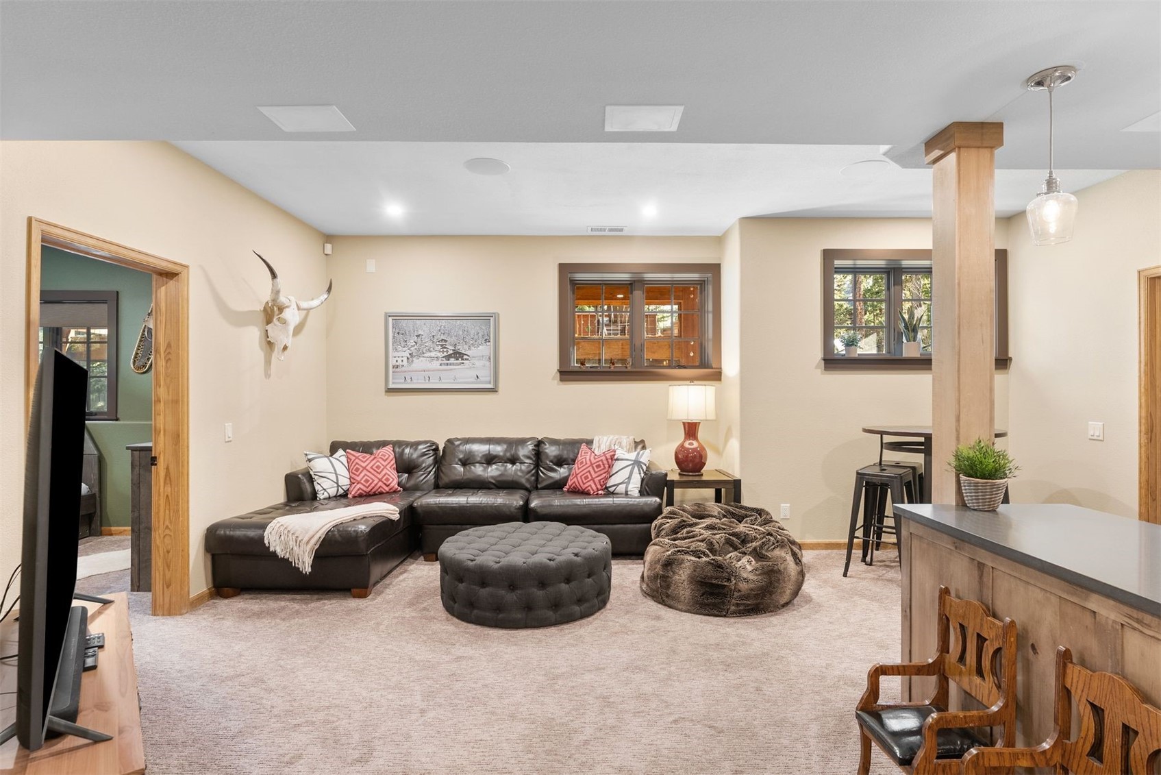 Furnished living room with a leather sectional, tufted ottoman, and bar counter.