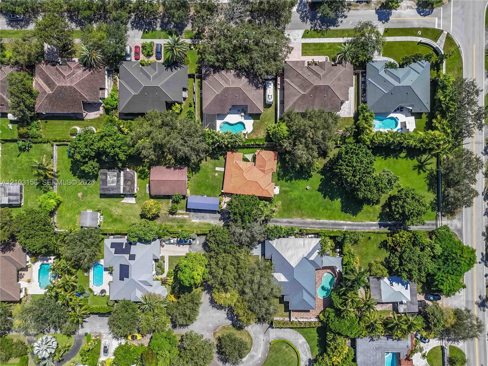 Aerial view of a tree-lined South Miami property with an orange-tile-roof home and spacious grounds.
