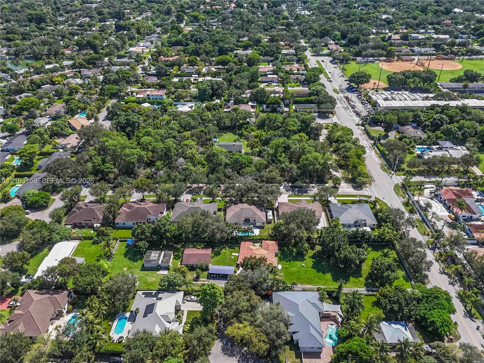 Aerial view of a tree-lined South Miami neighborhood, with homes, a baseball field, and a major intersection.