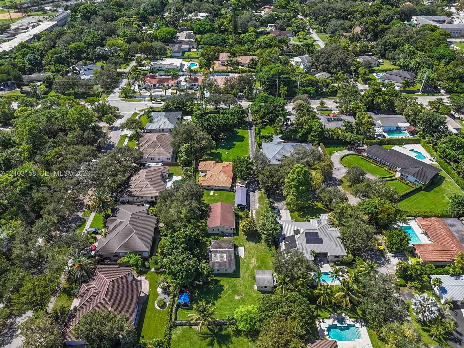 Aerial view of a leafy South Miami neighborhood with detached homes, swimming pools, and a cross street.