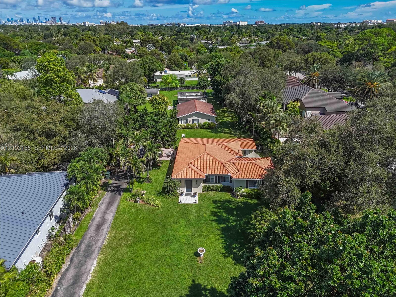 Aerial view of a South Miami home with a terracotta tile roof, broad lawn, and tree-lined surroundings.