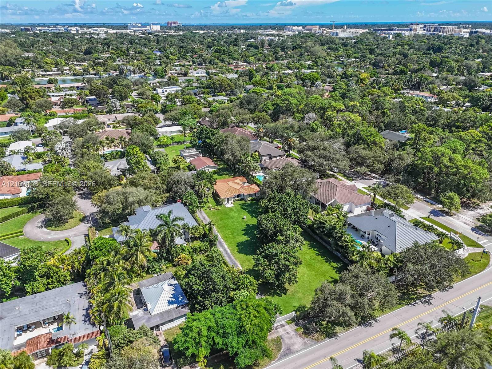 Aerial view of the property and leafy neighborhood, with a broad lawn and distant ocean horizon.