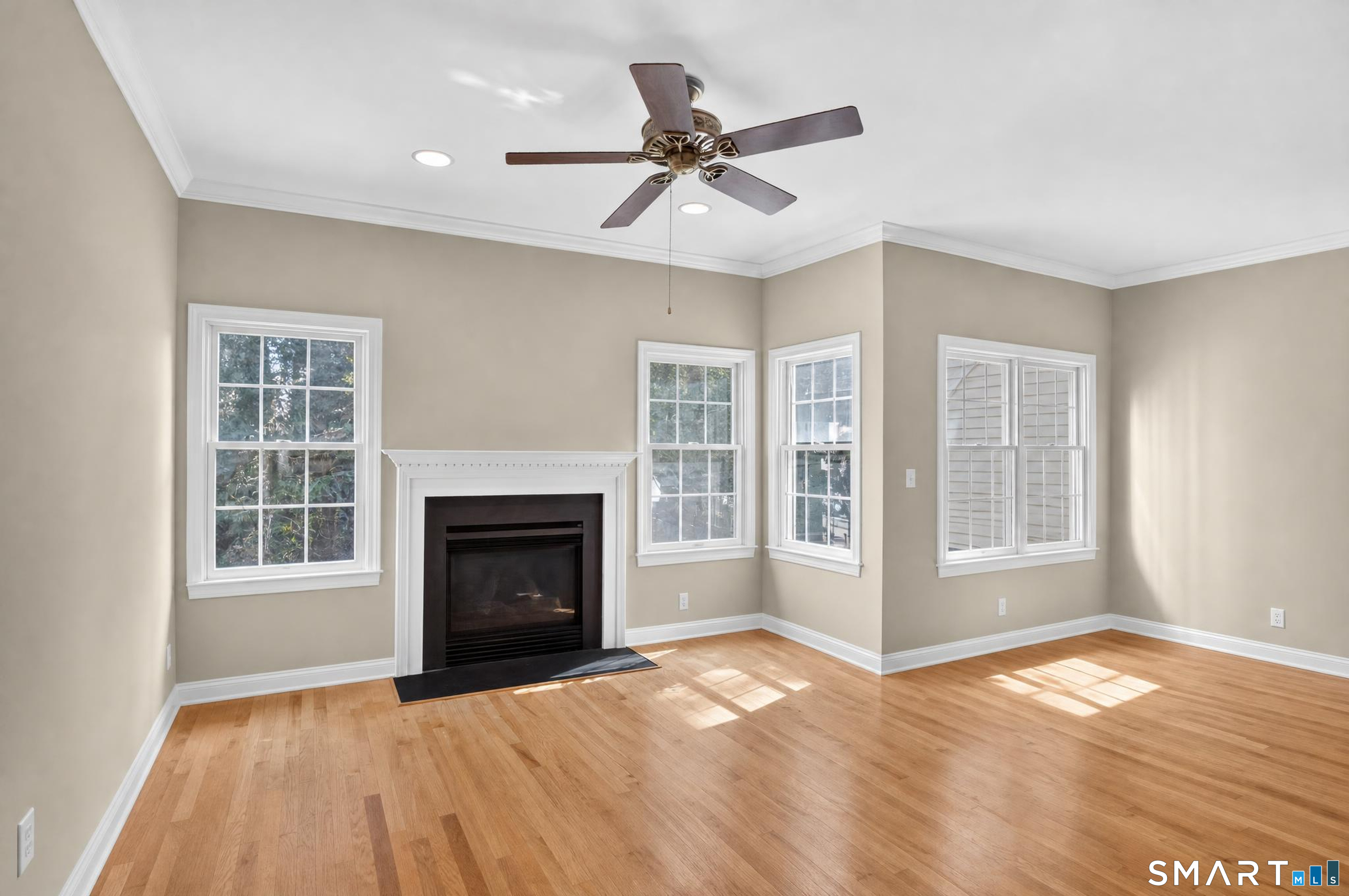Vacant living room with a black fireplace, hardwood floors, and multiple sunlit windows.